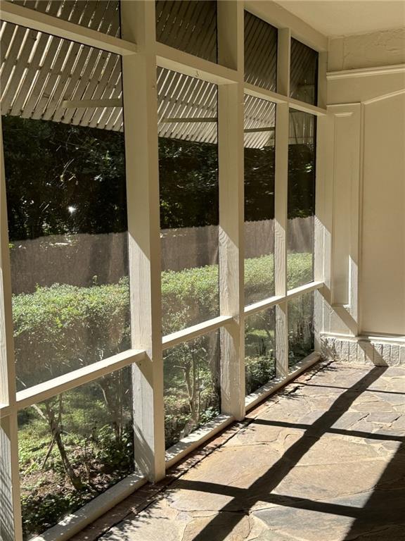 Enclosed sunroom with tall windows, leafy views, and a sunlit flagstone floor.