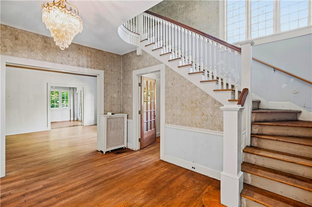 Entry hall with a white staircase, hardwood floors, tall windows, and a chandelier.