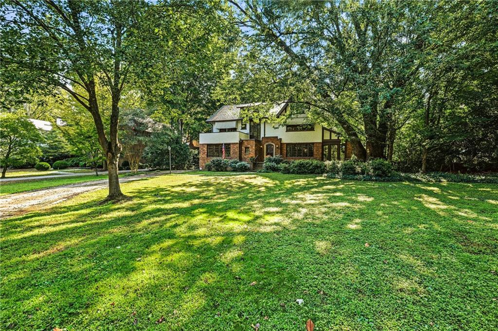 Two-story brick and siding house beyond a broad lawn, framed by mature trees.