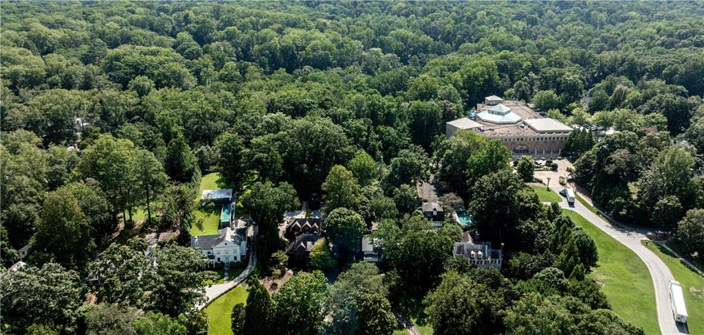 Aerial view of homes among dense trees, with a large building and curving road.
