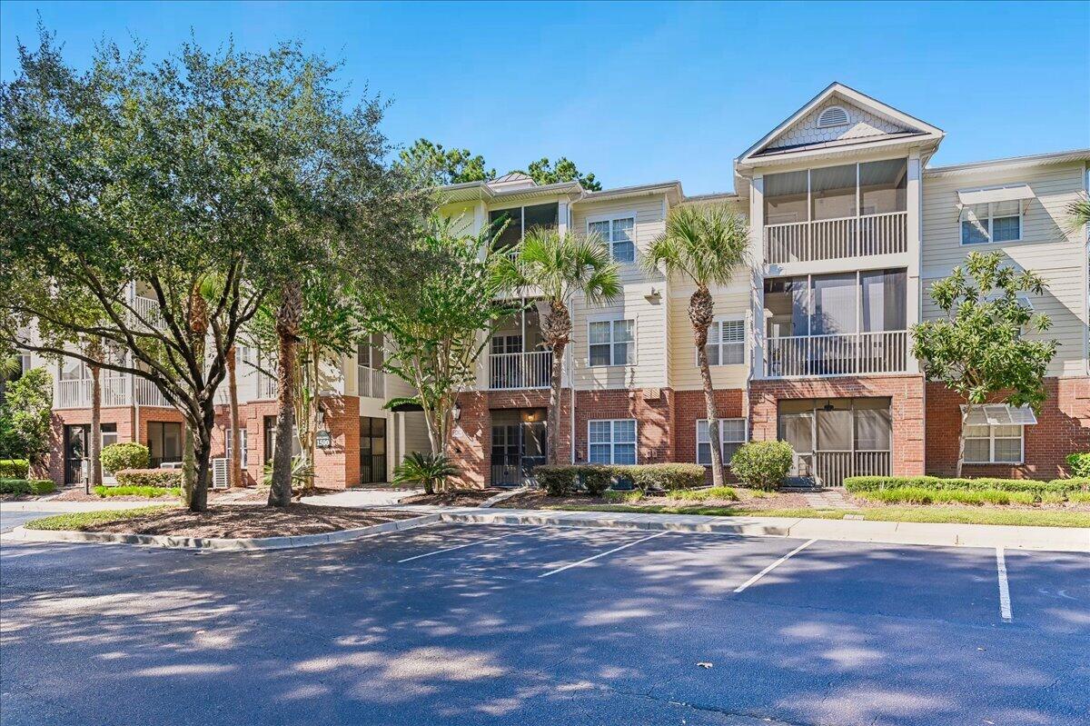 Multi-story residential building with screened balconies, palm trees, and a parking lot in front.