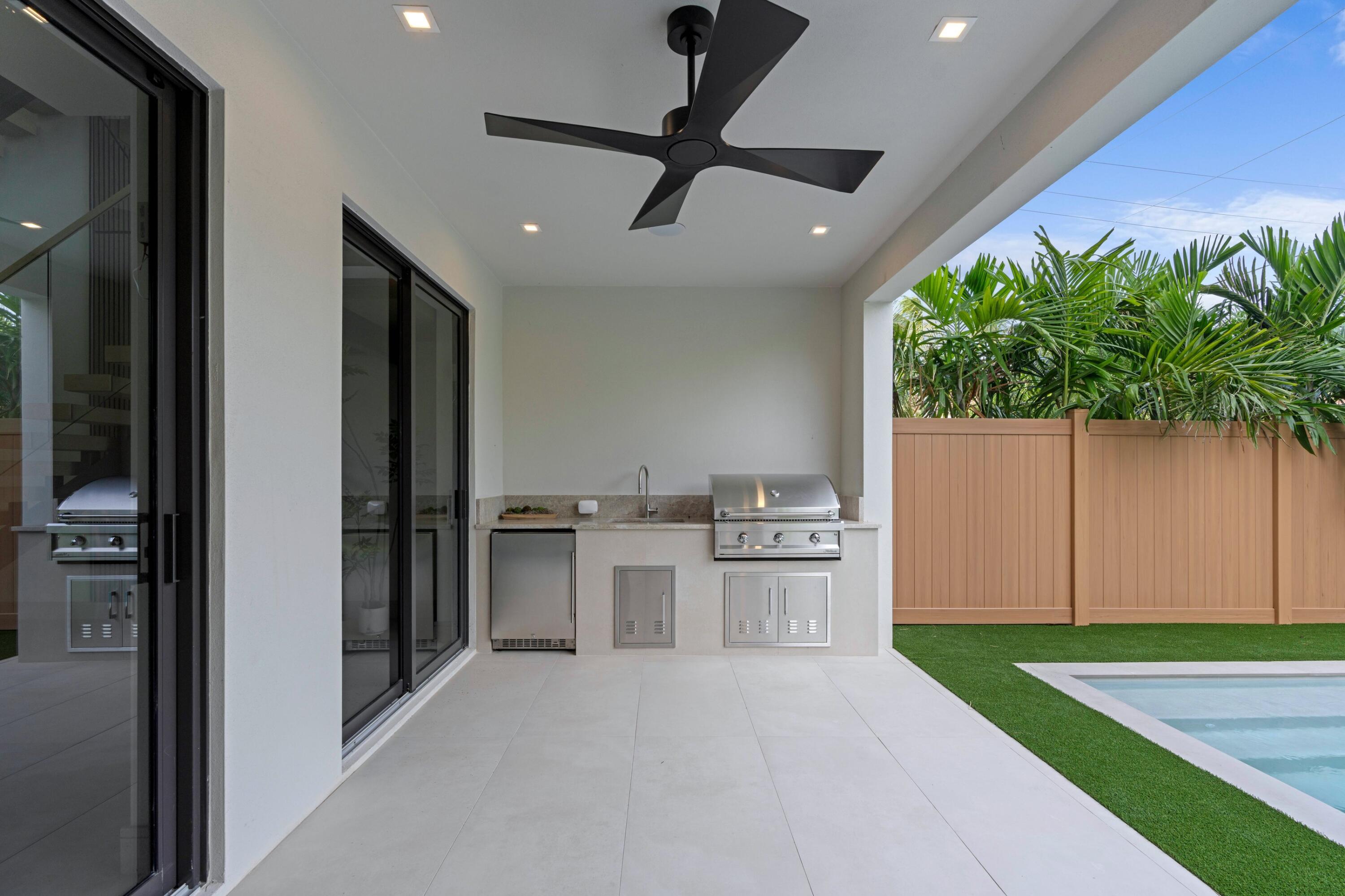 Covered outdoor kitchen with stainless grill beside a backyard pool.