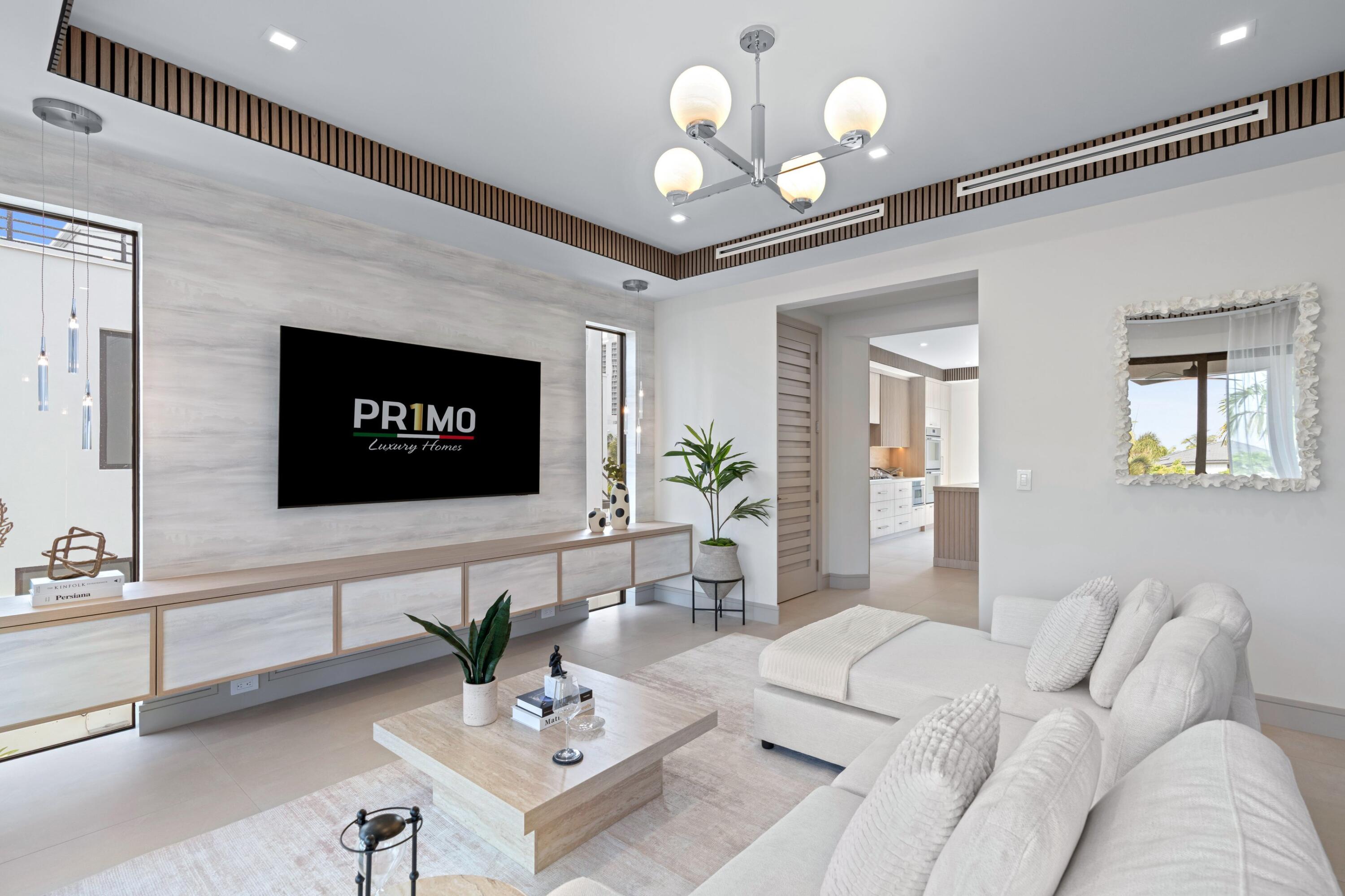 Bright living room with white sofas, a marble coffee table, and a TV wall beside the kitchen.