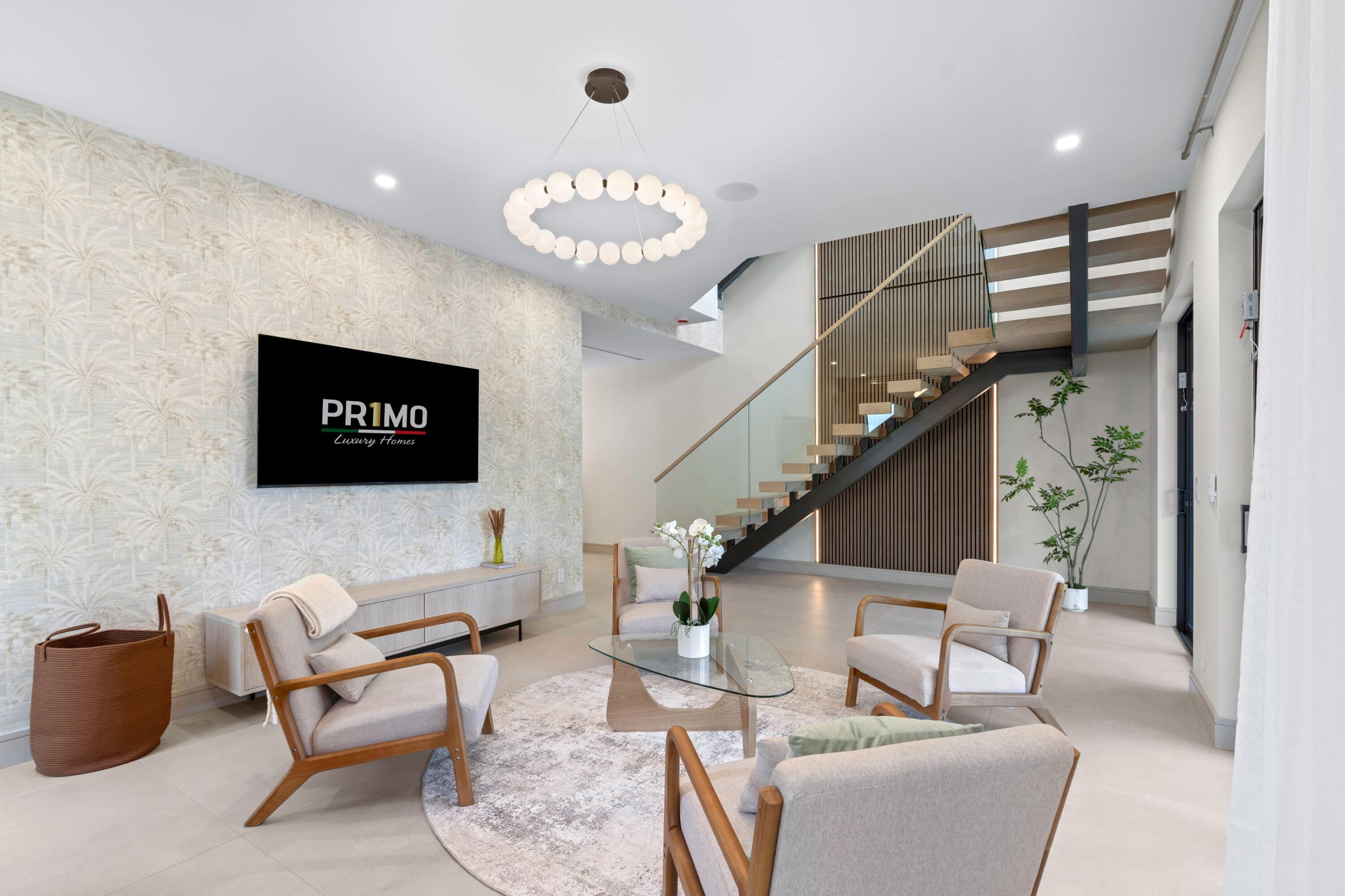 Furnished living room with sculptural staircase, palm-patterned wallpaper, and circular chandelier.