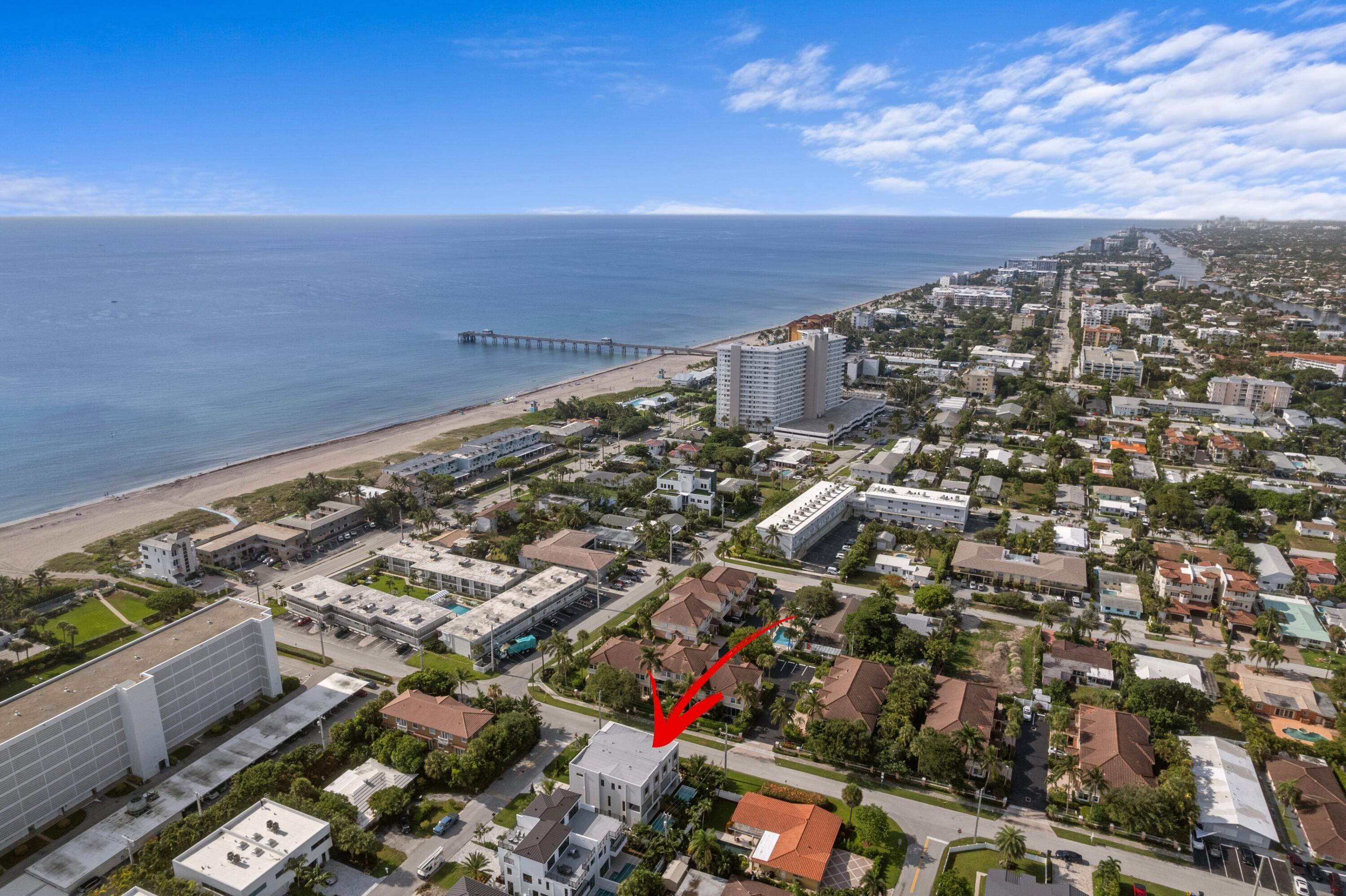 Aerial view of the property marked by a red arrow, with the beach and ocean beyond.