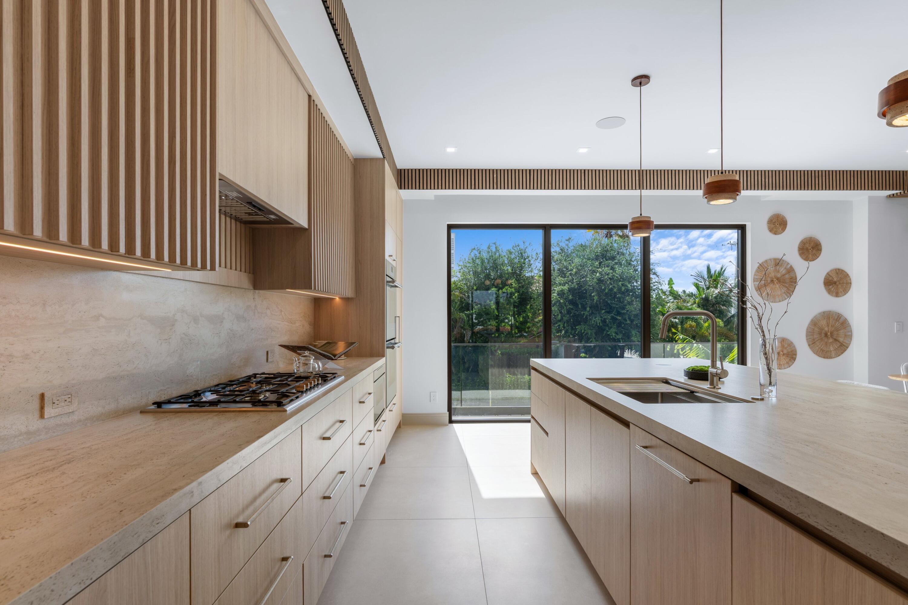 Modern kitchen with wood cabinetry, a large island, and sliding glass doors to a leafy garden.