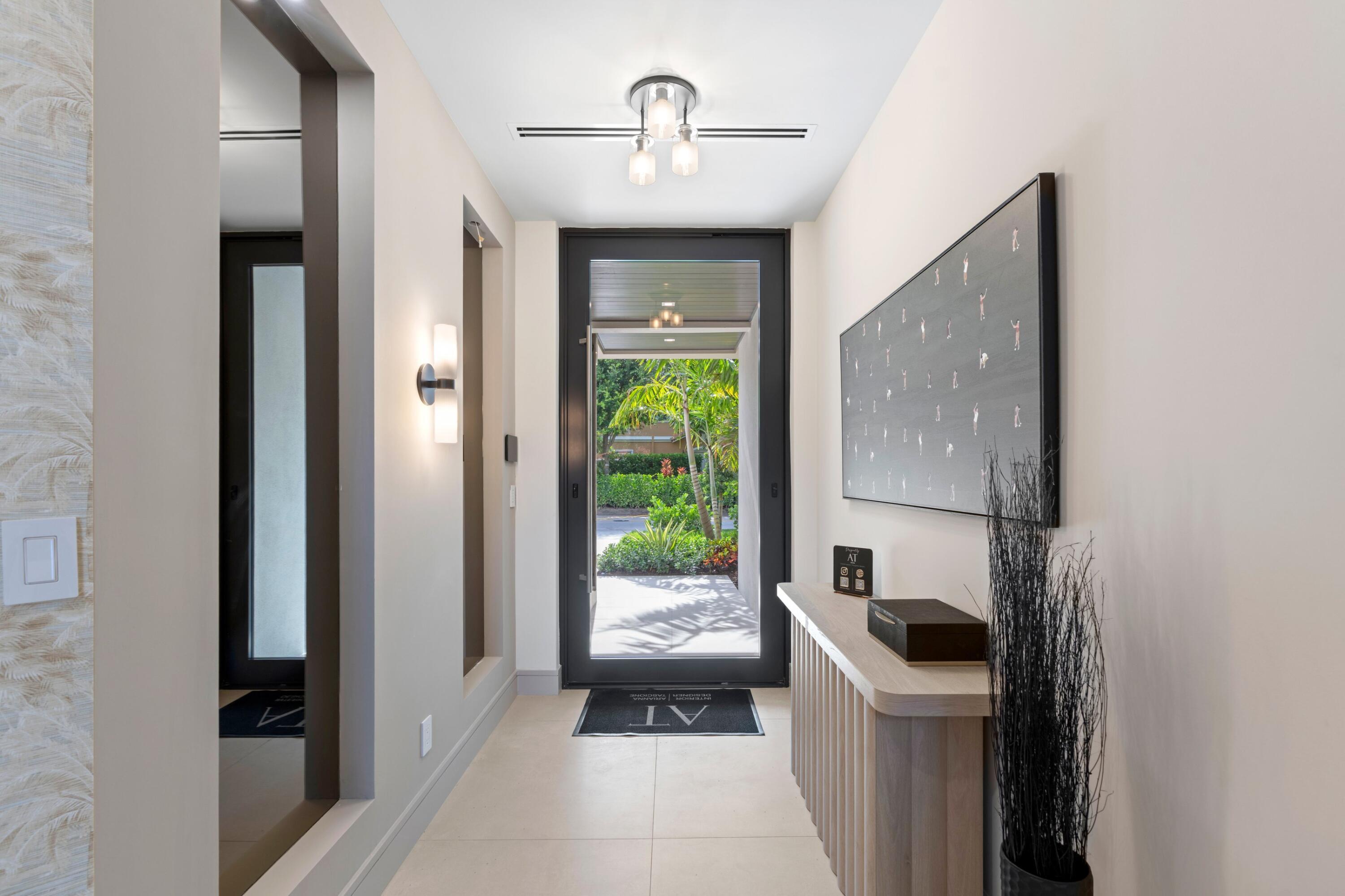 Bright entry hallway with a fluted console, modern lighting, and a glass front door opening to tropical landscaping.