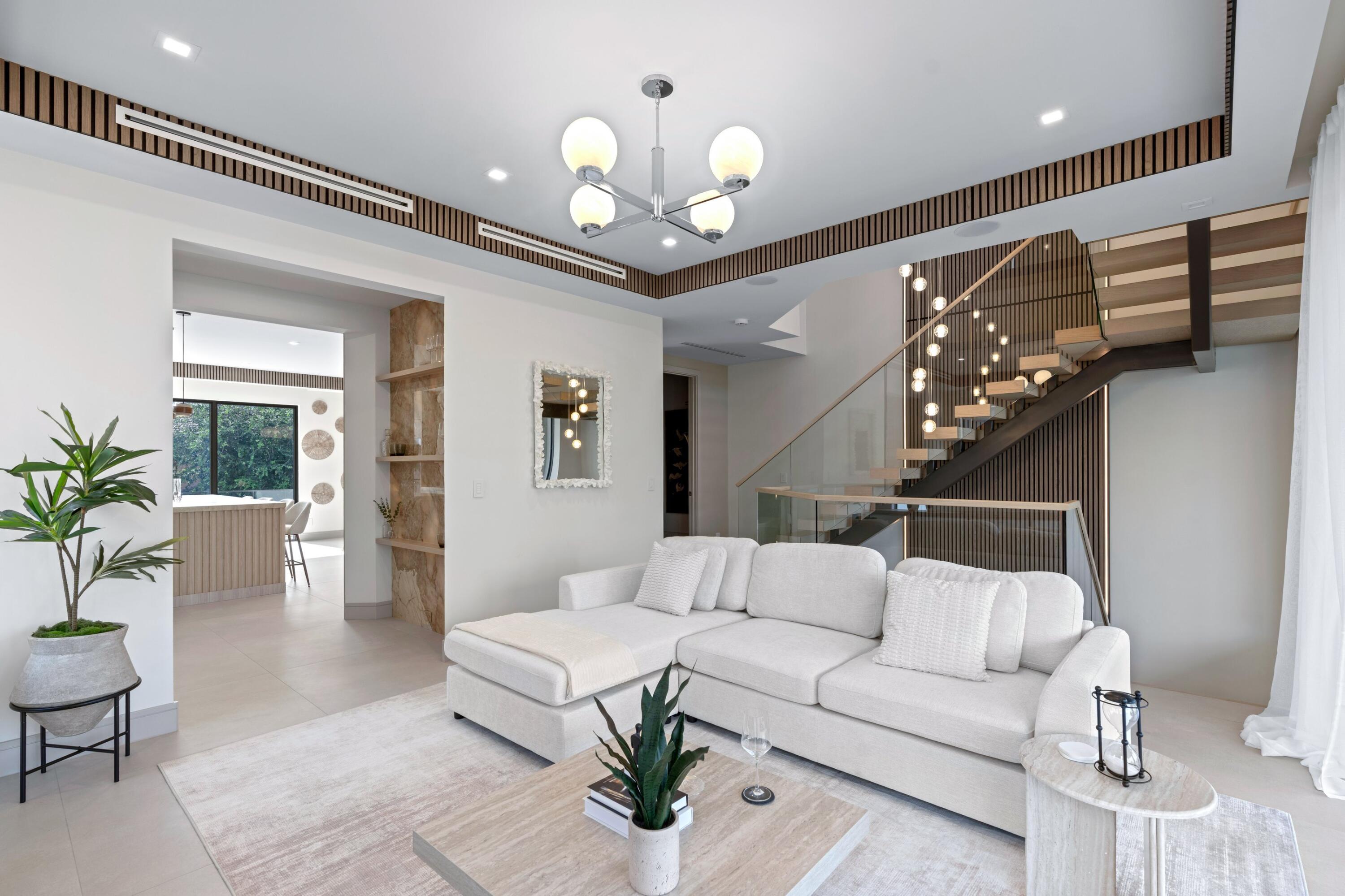 Bright living room with white sectional sofa, marble coffee table, and sculptural open staircase.