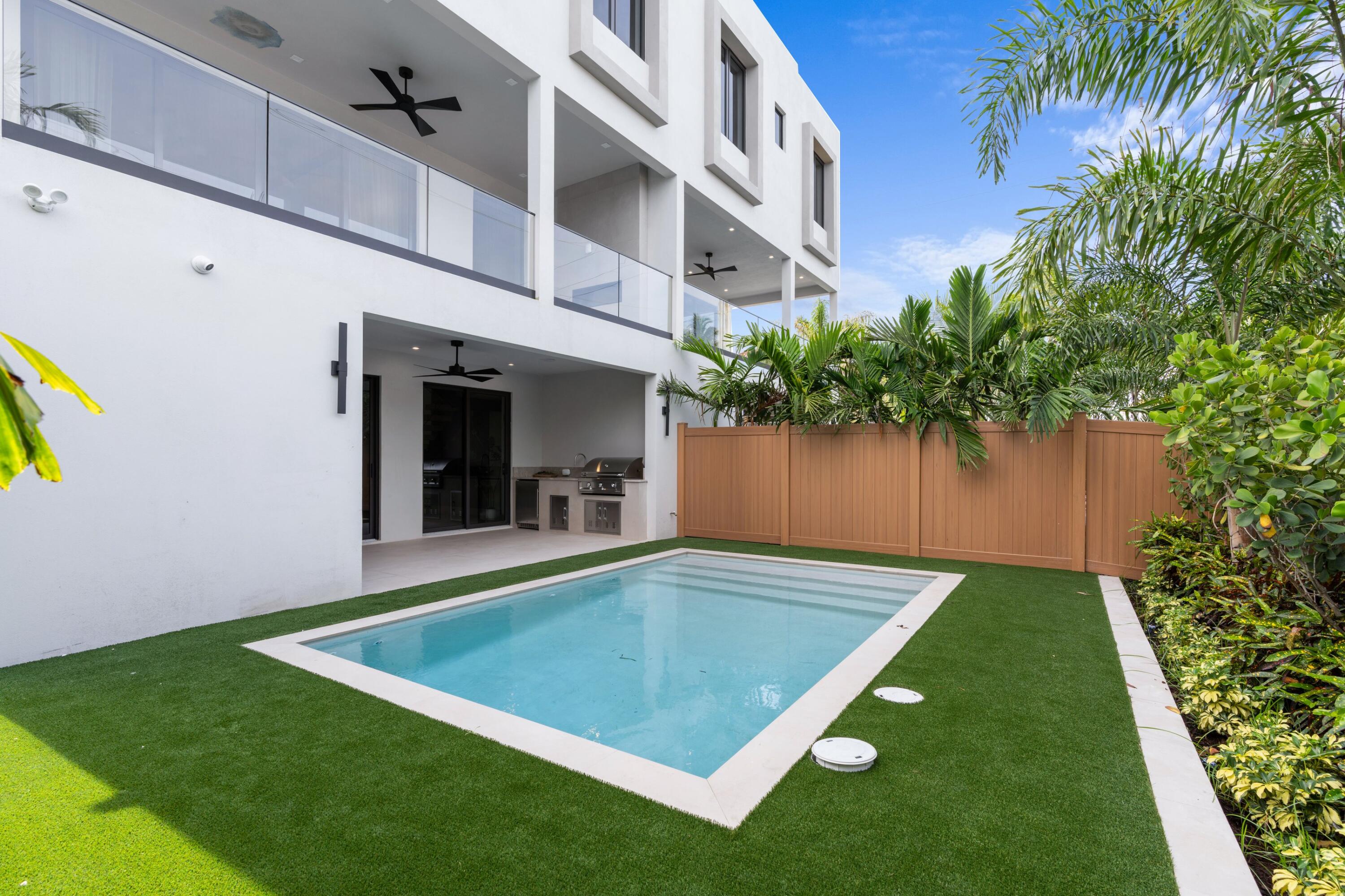 Modern white home with a rectangular pool, covered patio, and tropical landscaping.