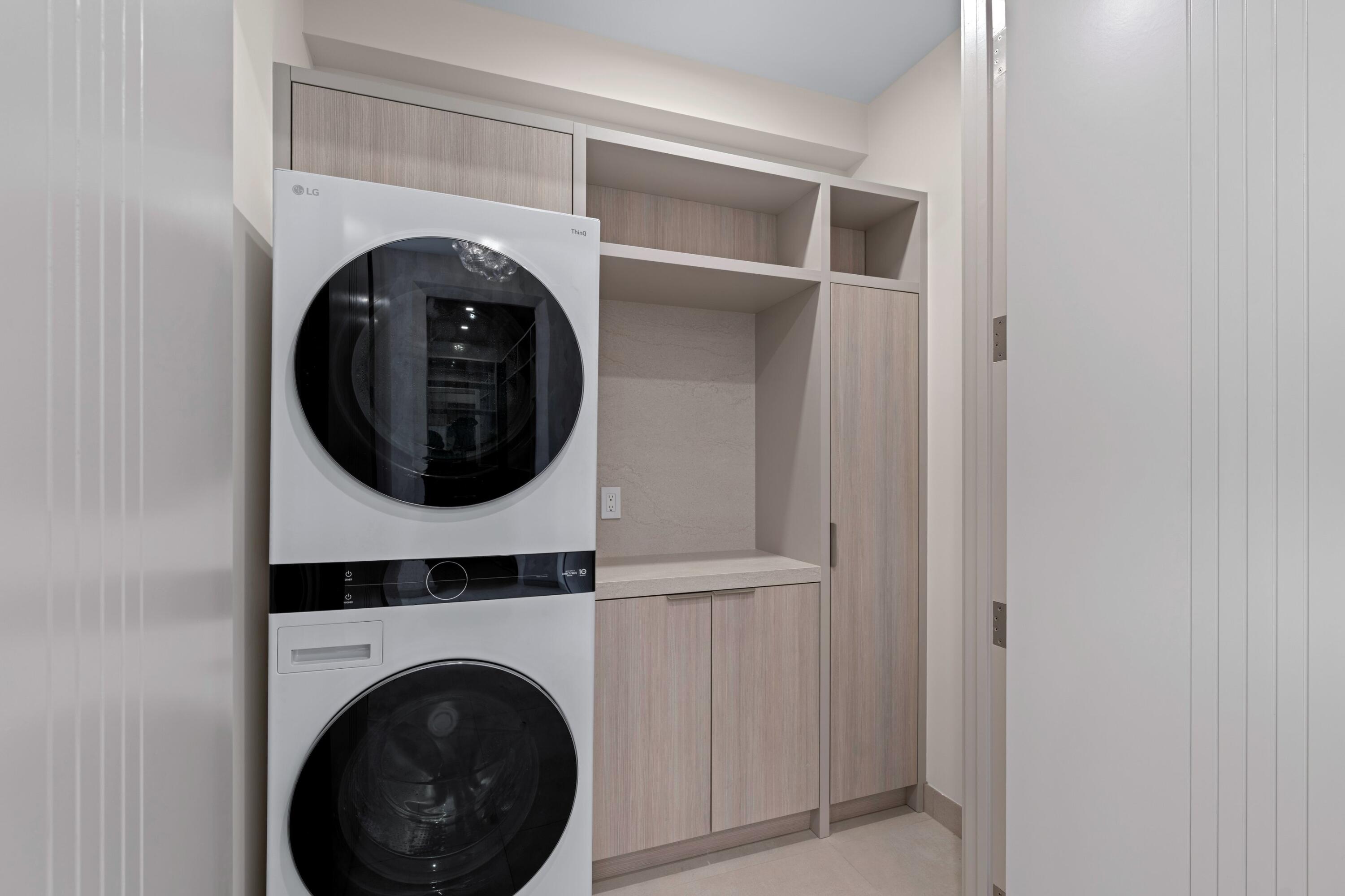Laundry room with stacked front-loading washer and dryer beside built-in cabinets and a utility counter.