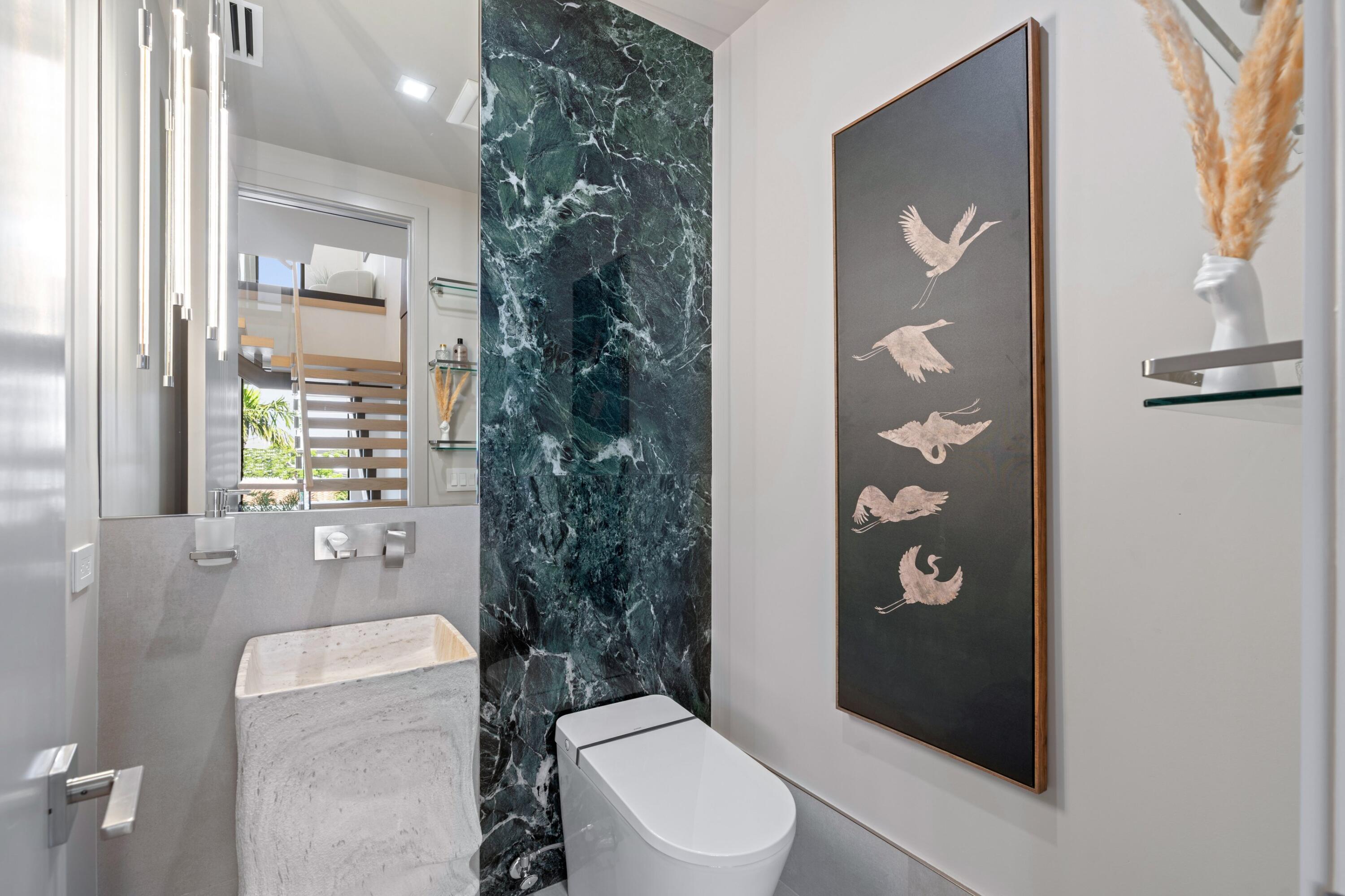 Powder room with a sculptural stone sink, green marble accent wall, and framed bird artwork.