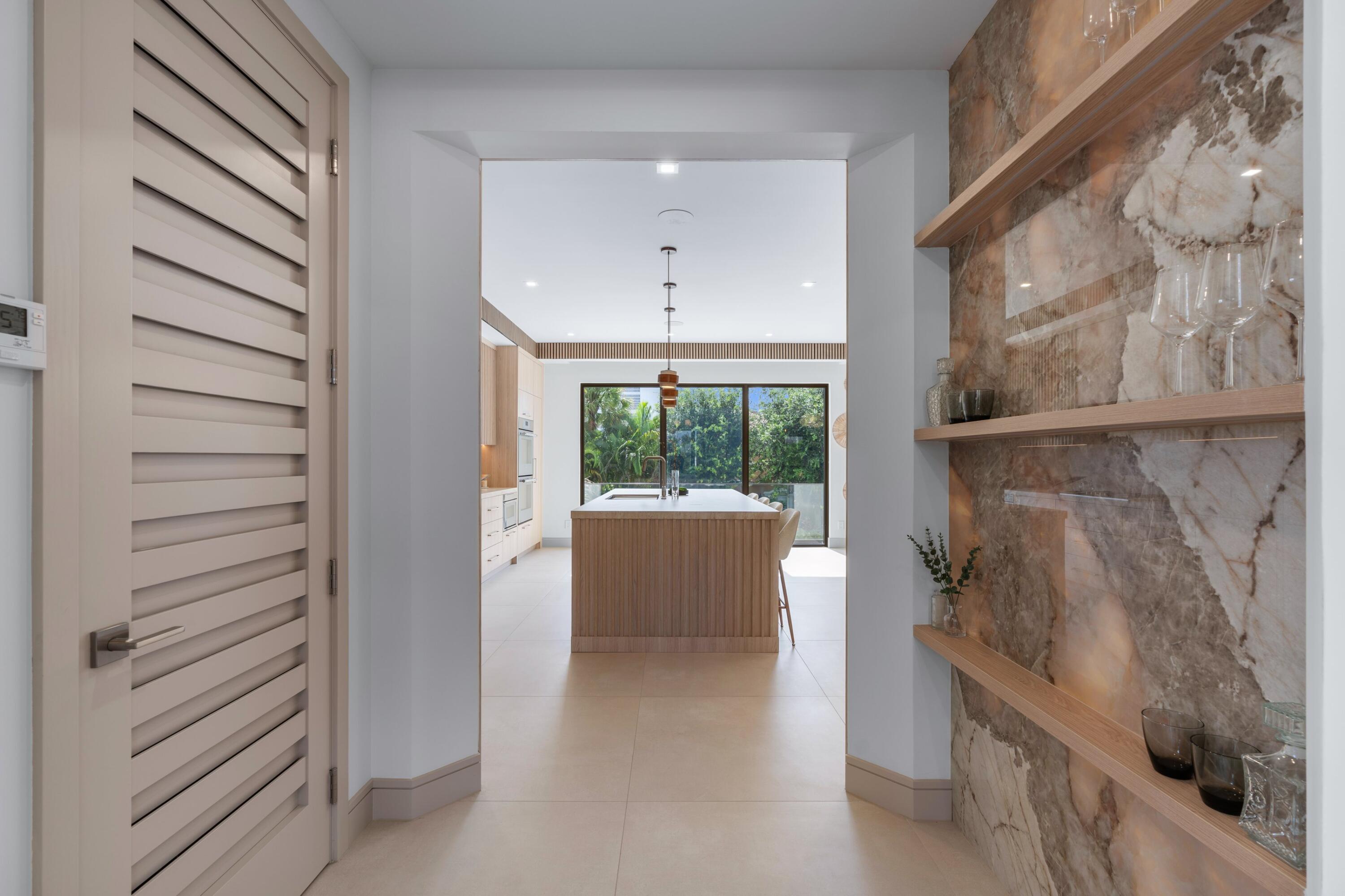 Modern kitchen with a wood-front island, marble display shelves, and garden views through glass doors.