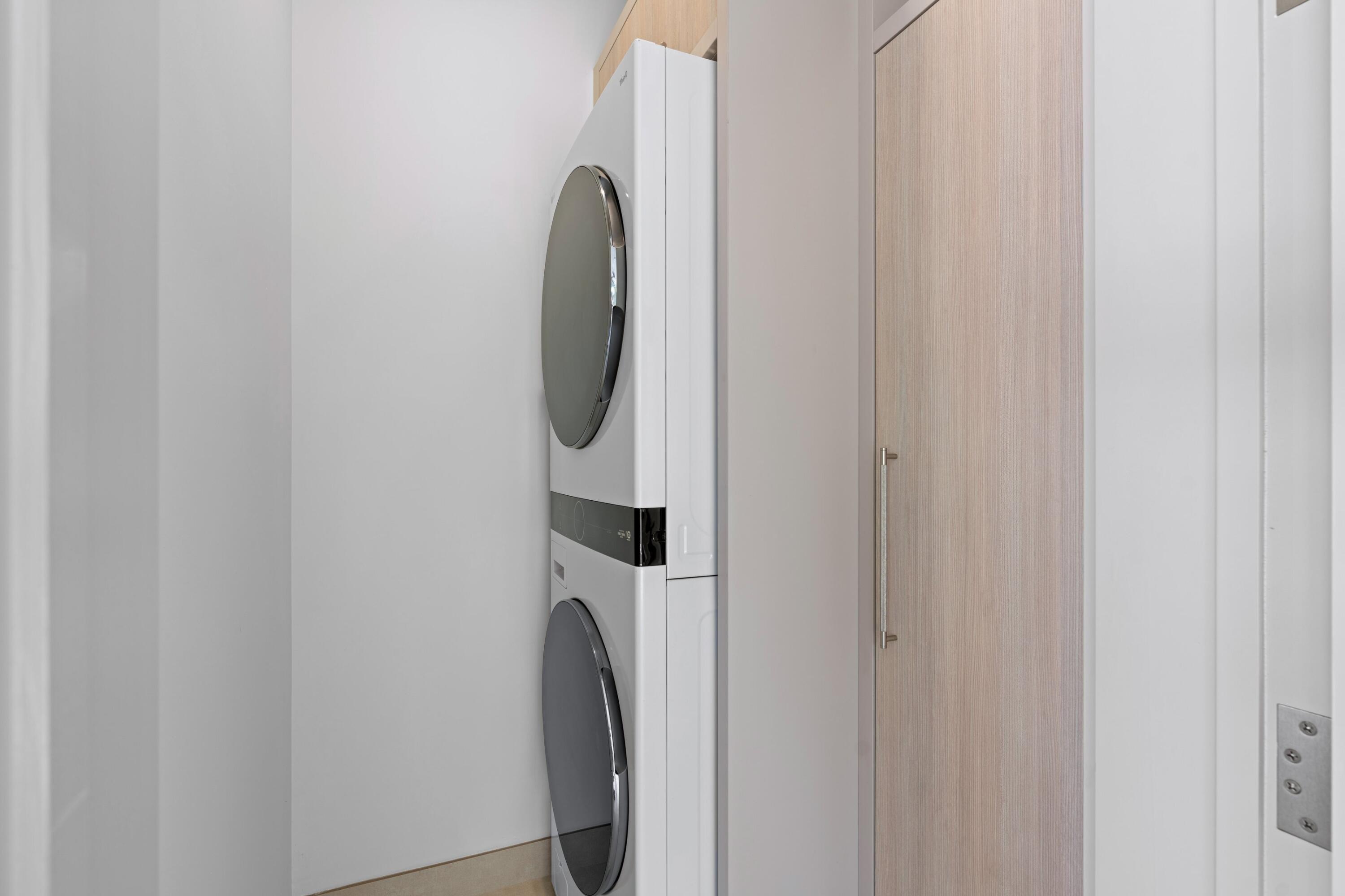 Laundry area with a stacked white washer and dryer beside a light wood door.