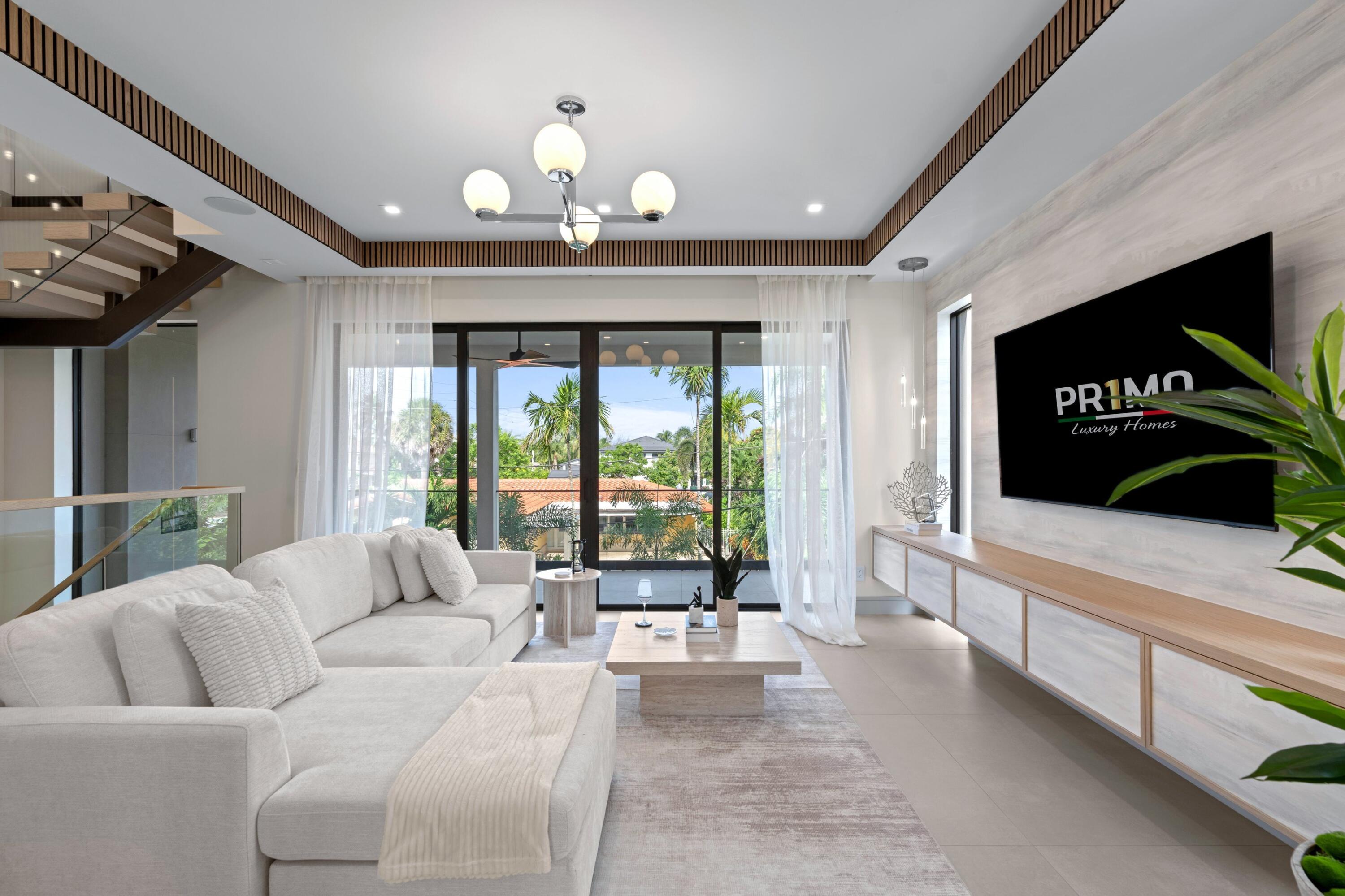 Bright living room with white sectional sofa, glass doors, and a view of palm trees.