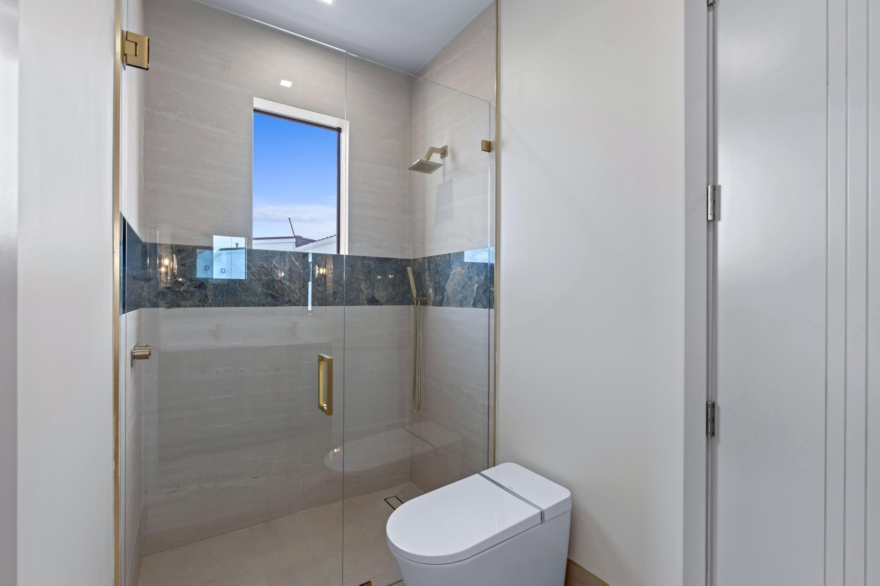 Modern bathroom with a glass-enclosed shower, dark marble accent band, and wall-mounted toilet.