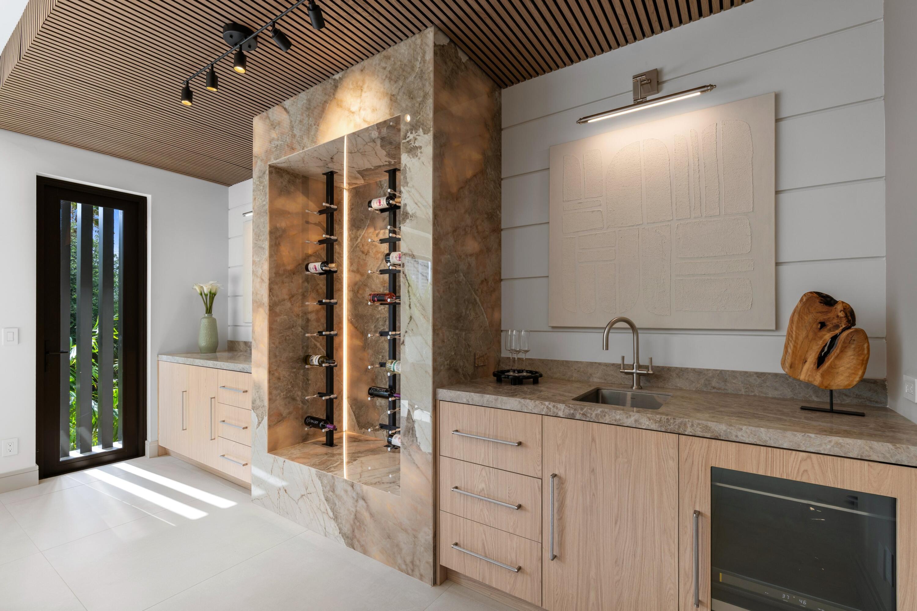 Home bar with a marble wine display, wood cabinetry, sink, and built-in beverage refrigerator.