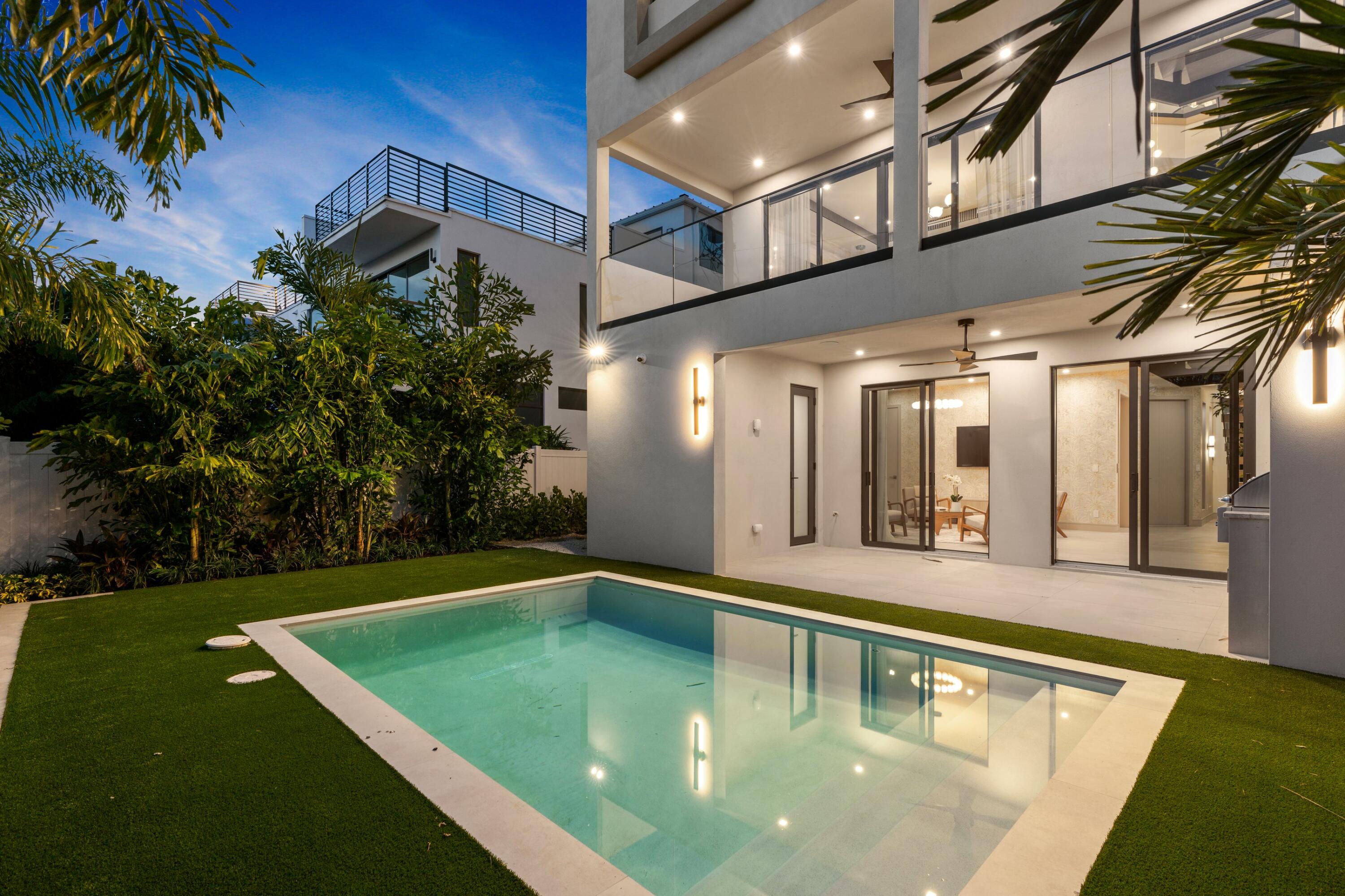 Modern two-story home beside a rectangular pool, with illuminated glass balconies at dusk.