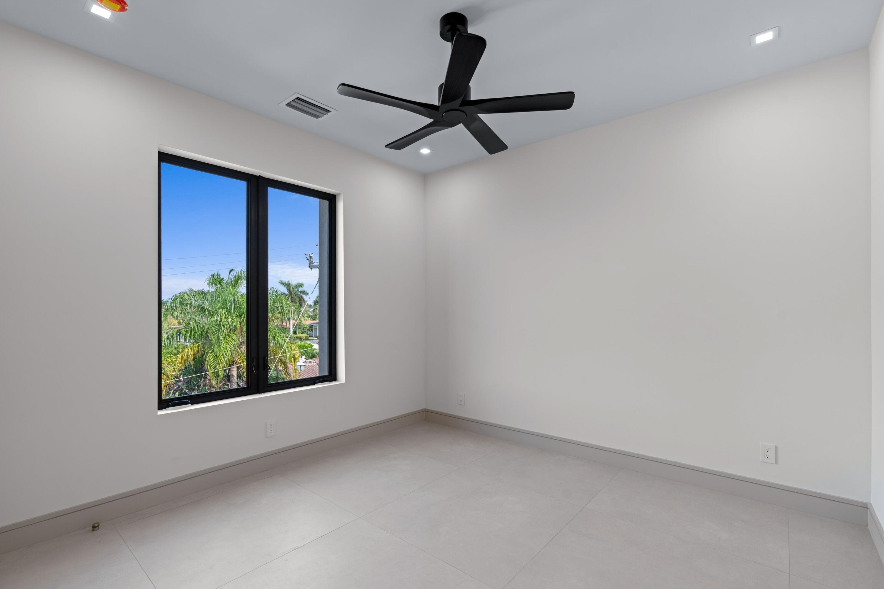 Empty room with a black ceiling fan, large window, and palm trees outside.