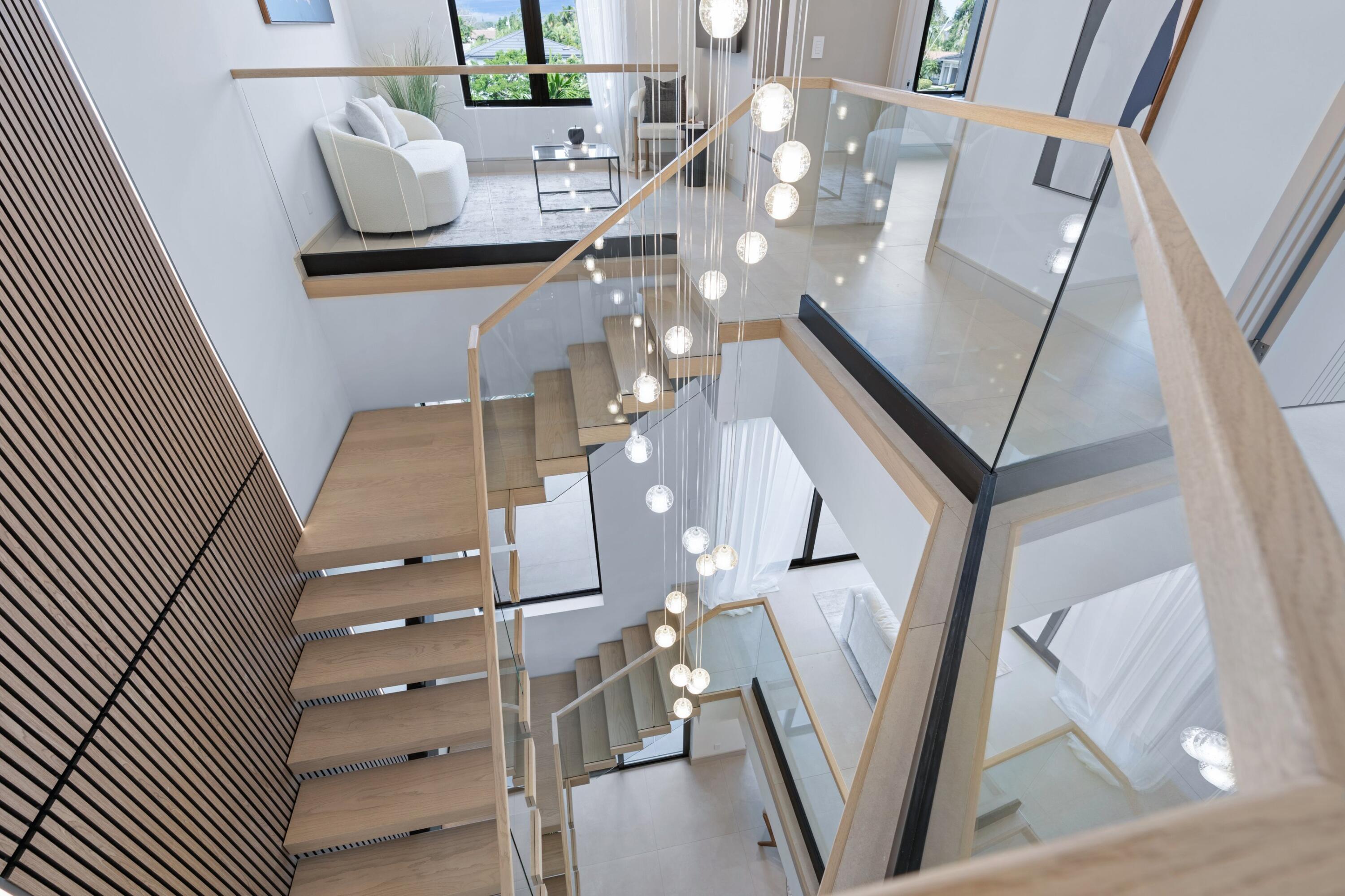 Open staircase with floating wood treads, glass railings, and a cascading globe chandelier.