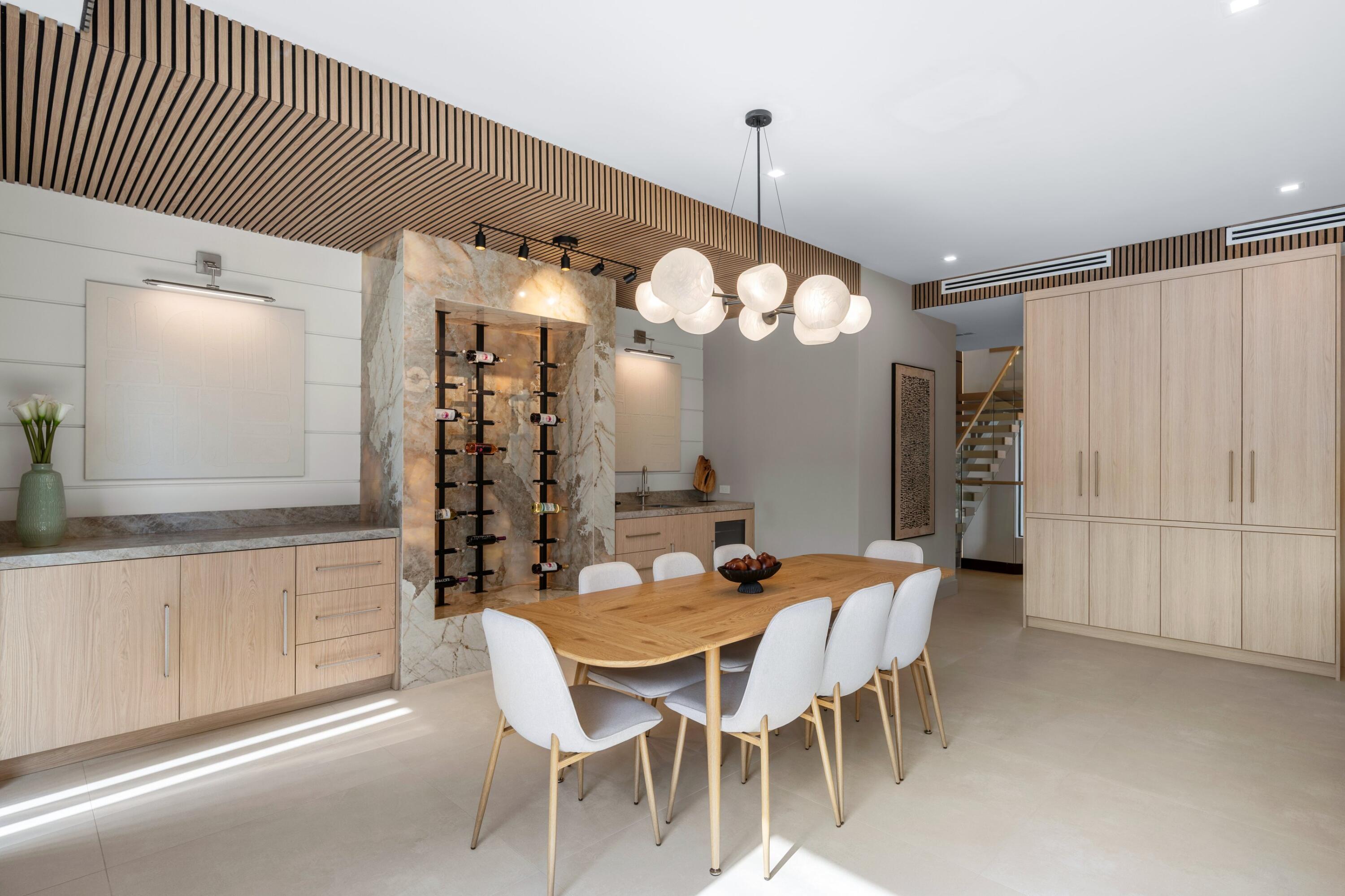 Dining room with a long wood table, sculptural marble wine display, and pale wood cabinetry.