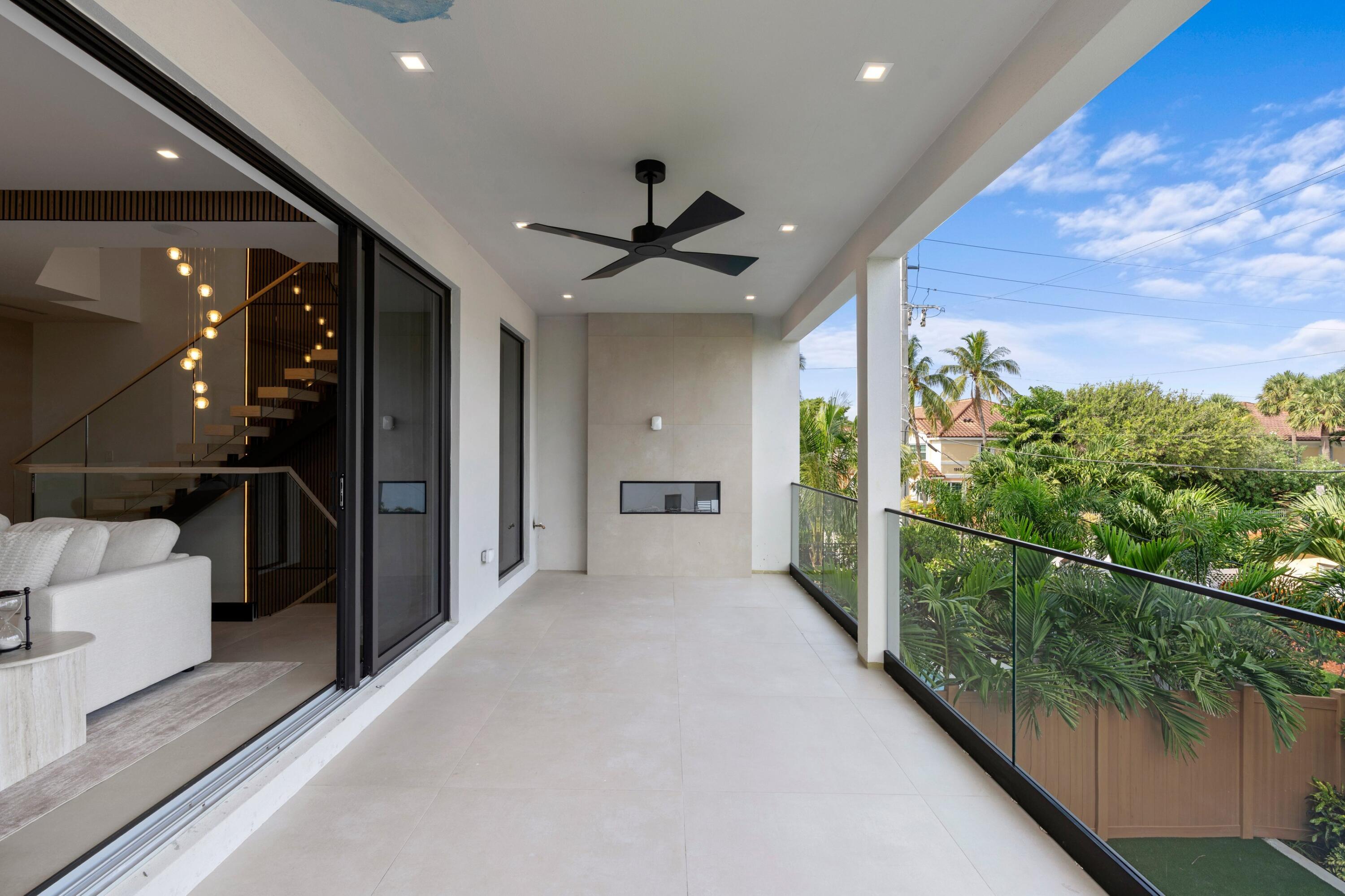 Covered balcony with glass railing, ceiling fan, and views of palm trees and neighboring homes.
