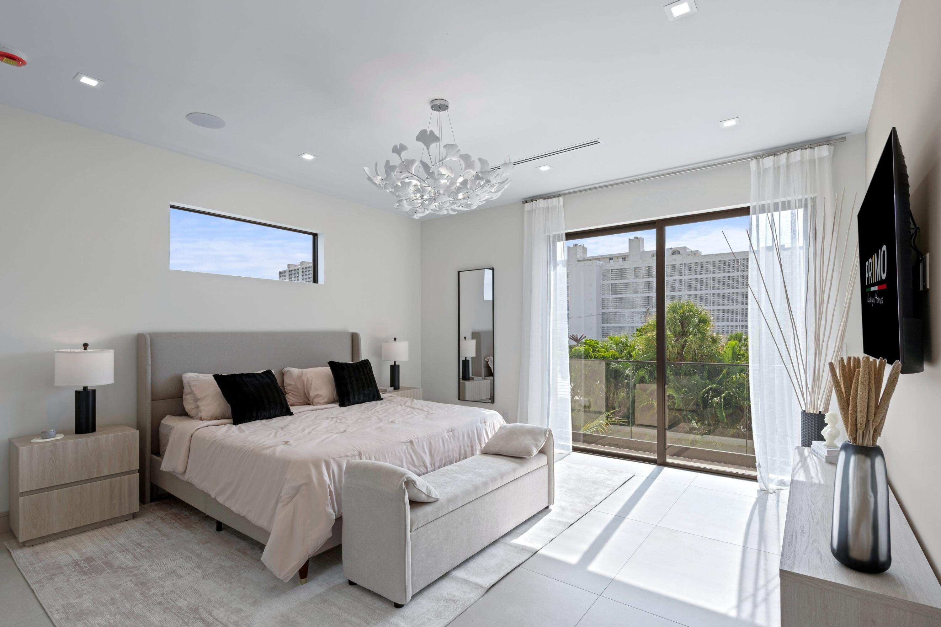 Staged bedroom with a king bed, sculptural chandelier, and sliding glass doors overlooking palm trees.