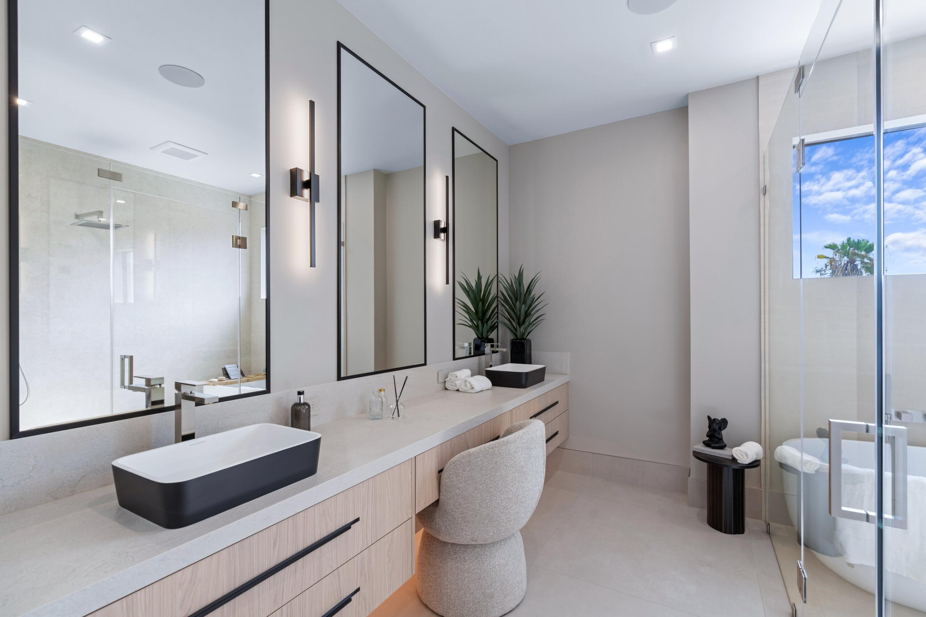 Modern bathroom with a long double vanity, black vessel sinks, and a glass-enclosed tub and shower.