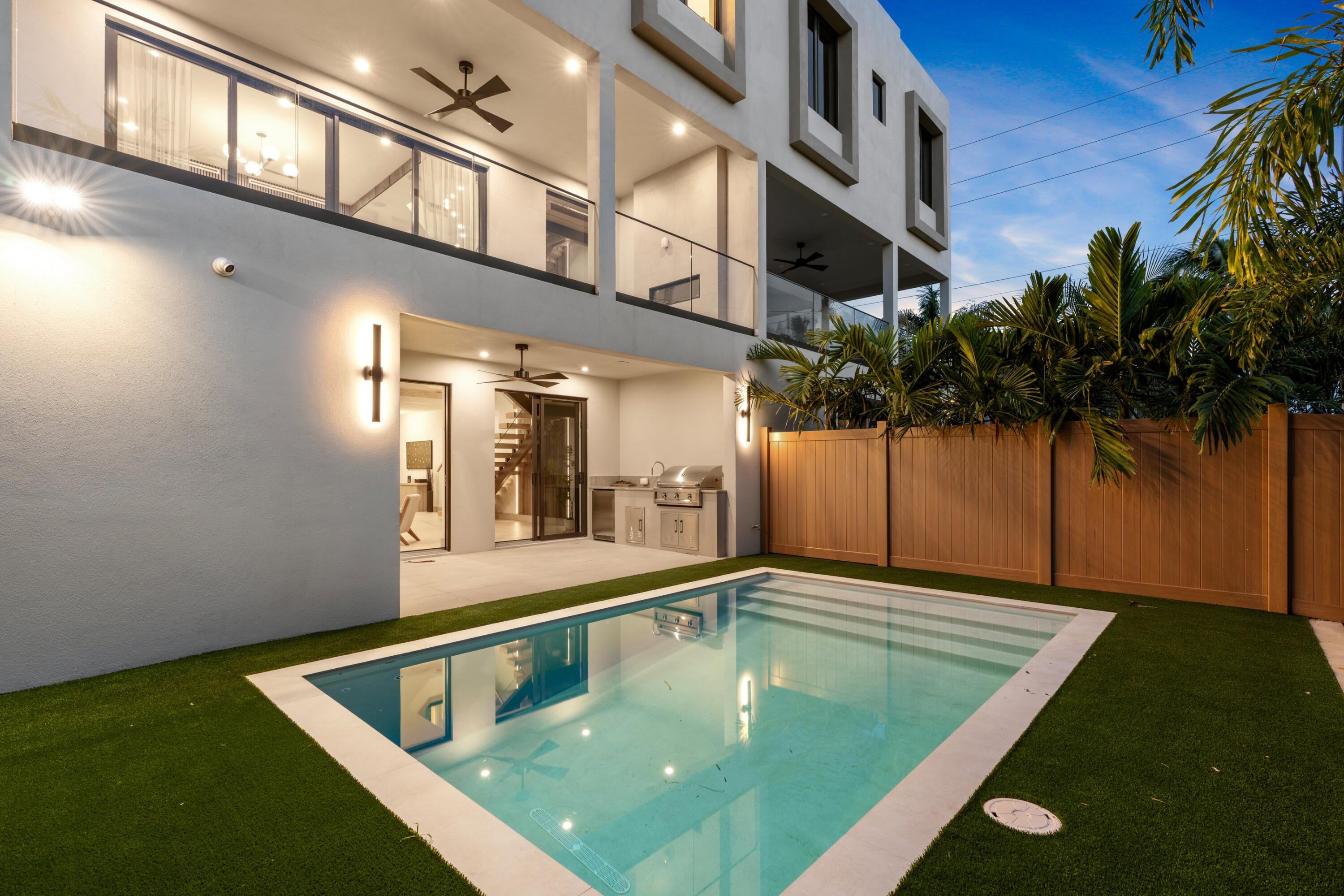 Modern white home with a rectangular pool, outdoor kitchen, and glass-railed balconies at dusk.