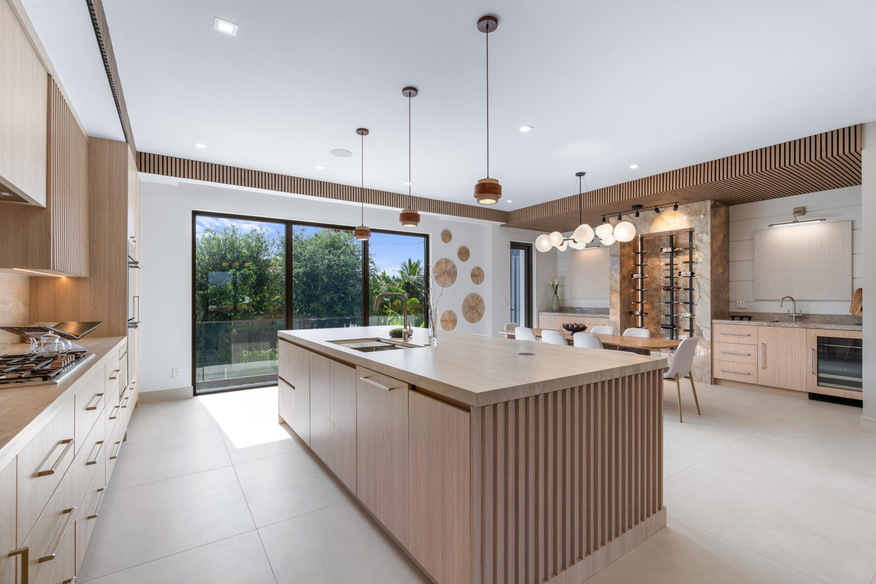 Modern kitchen with a large wood-slat island, dining area, and sliding glass doors to greenery.
