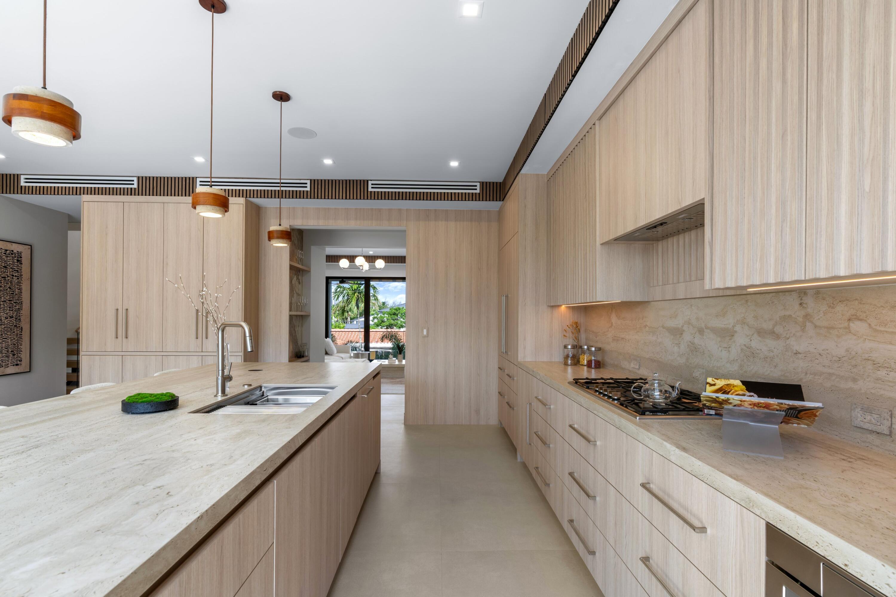 Modern kitchen with pale wood cabinetry, stone counters, and a large island with an integrated sink.