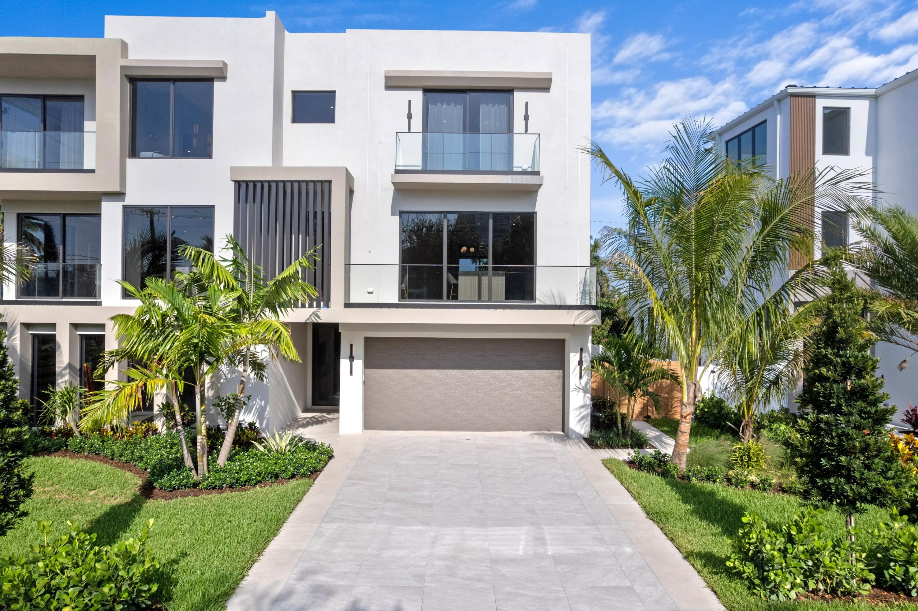 Modern white home with glass balconies, a double garage, and tropical landscaping.