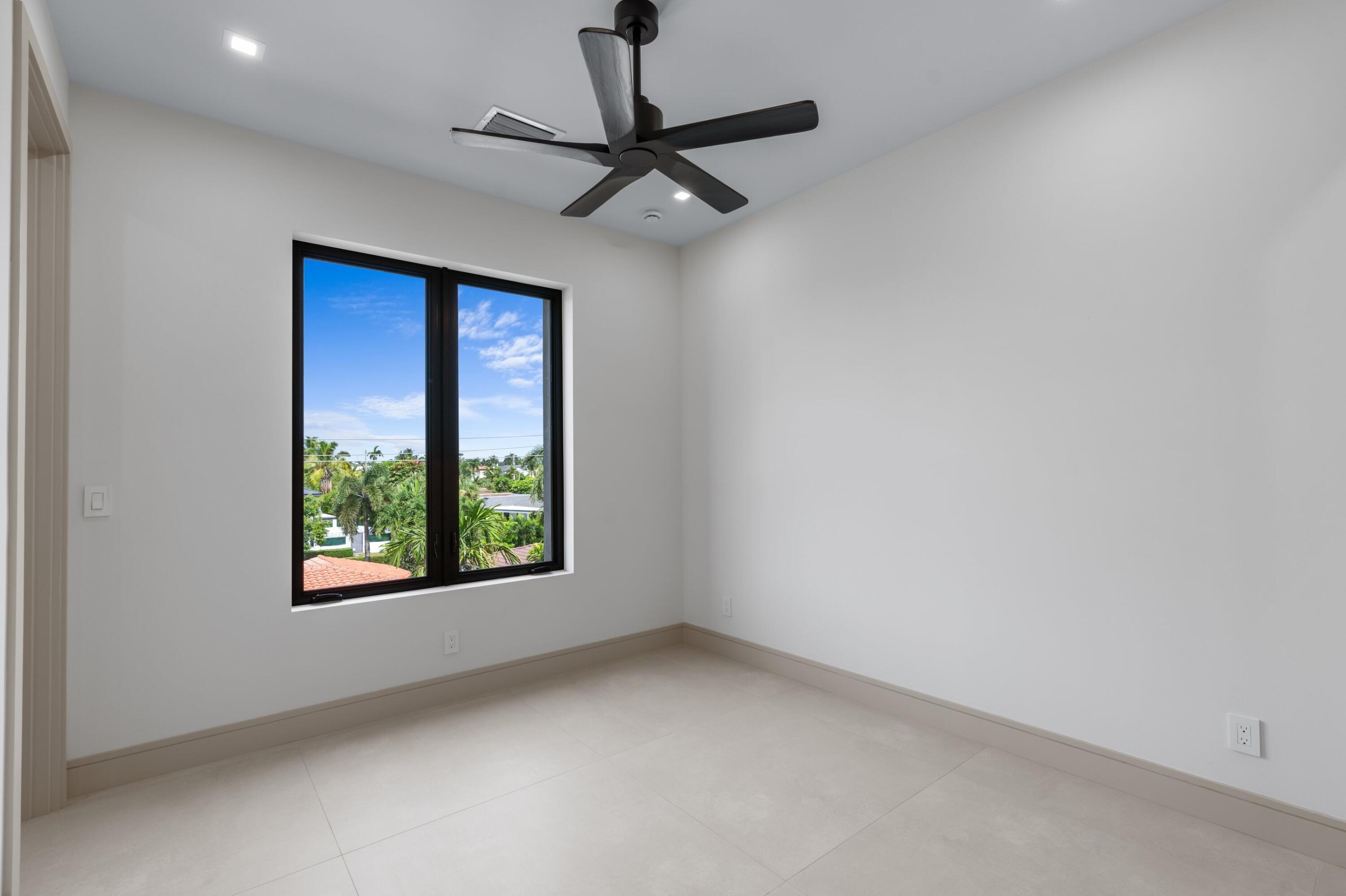Empty room with a black ceiling fan and a large window overlooking palm trees.