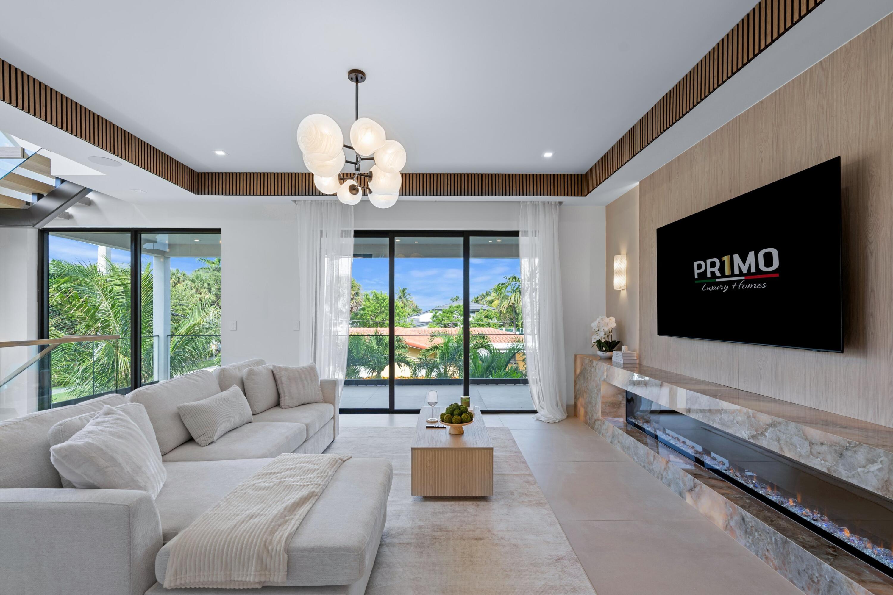 Living room with a marble fireplace, sculptural chandelier, and glass doors opening to tropical greenery.
