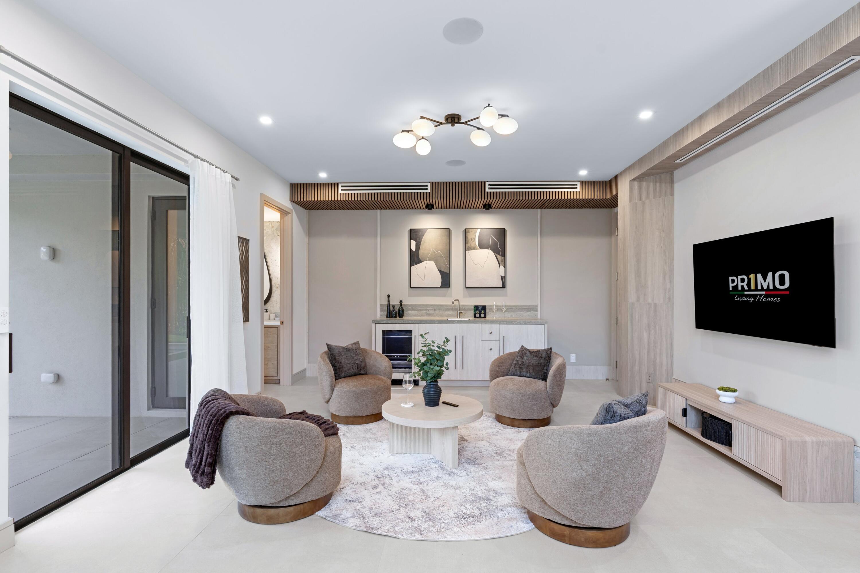 Living room with sculptural lounge chairs, a pale wood wet bar, and sliding glass doors.