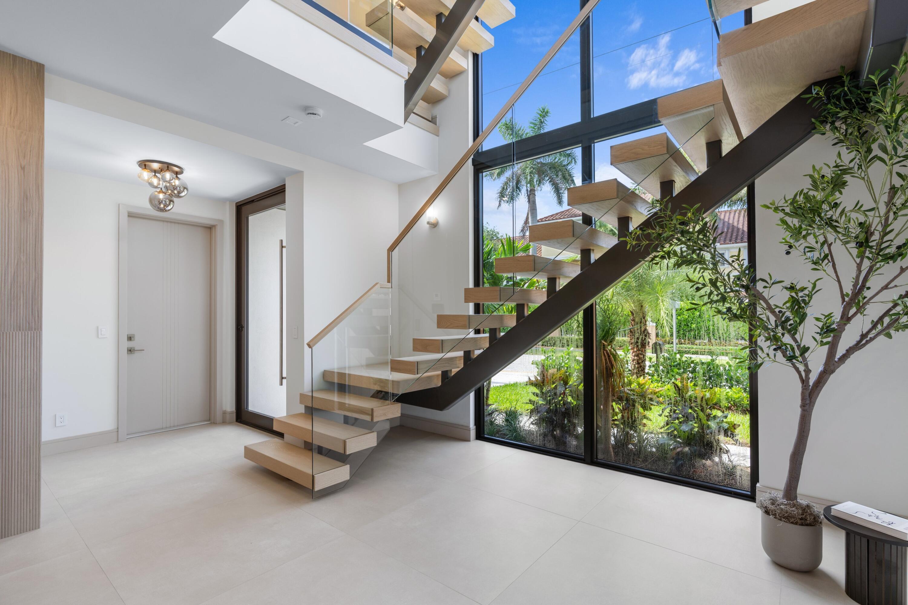 Bright entry foyer with a floating wood staircase, glass railing, and floor-to-ceiling garden windows.