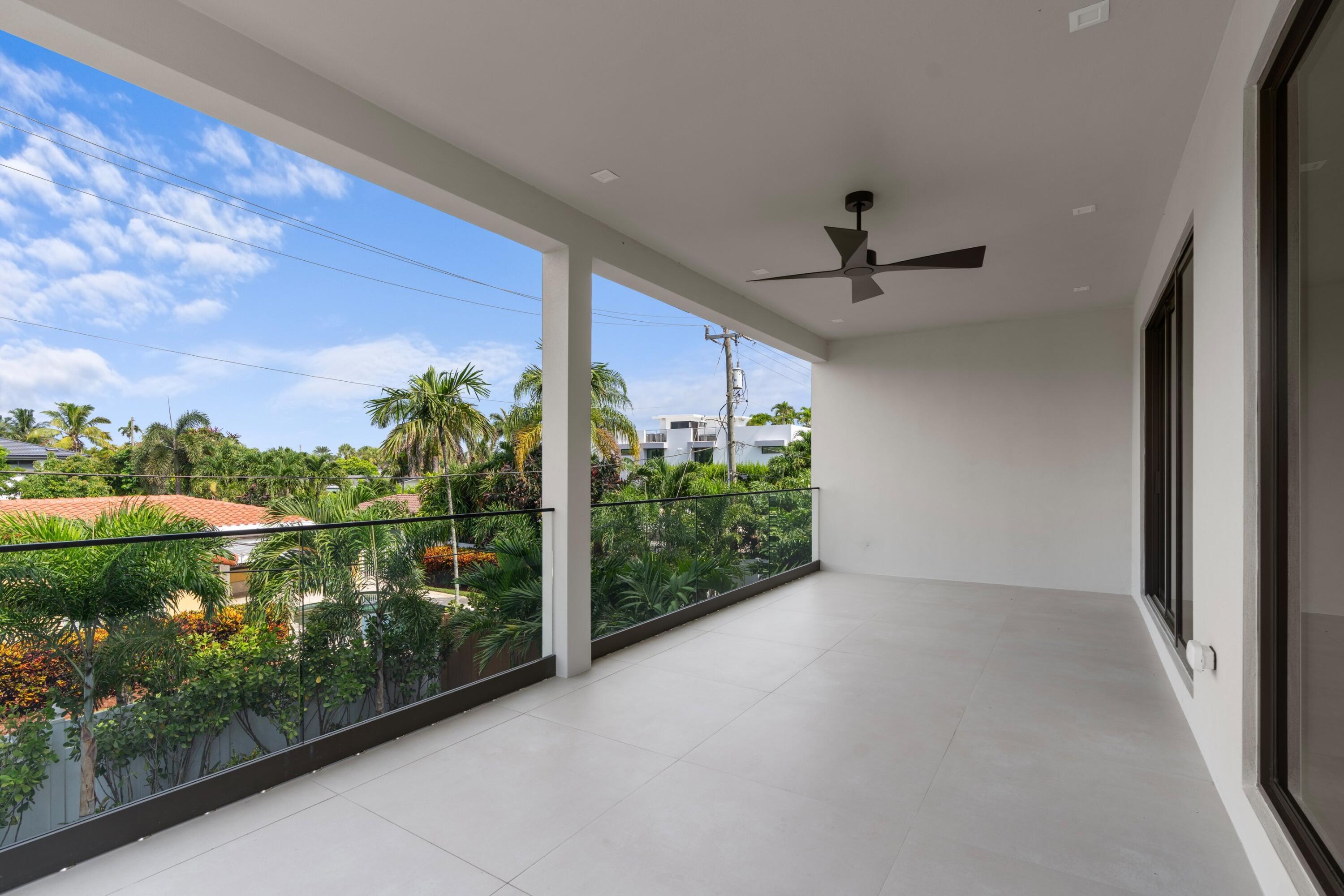 Covered balcony with glass railing, ceiling fan, and views of palm trees and neighboring homes.