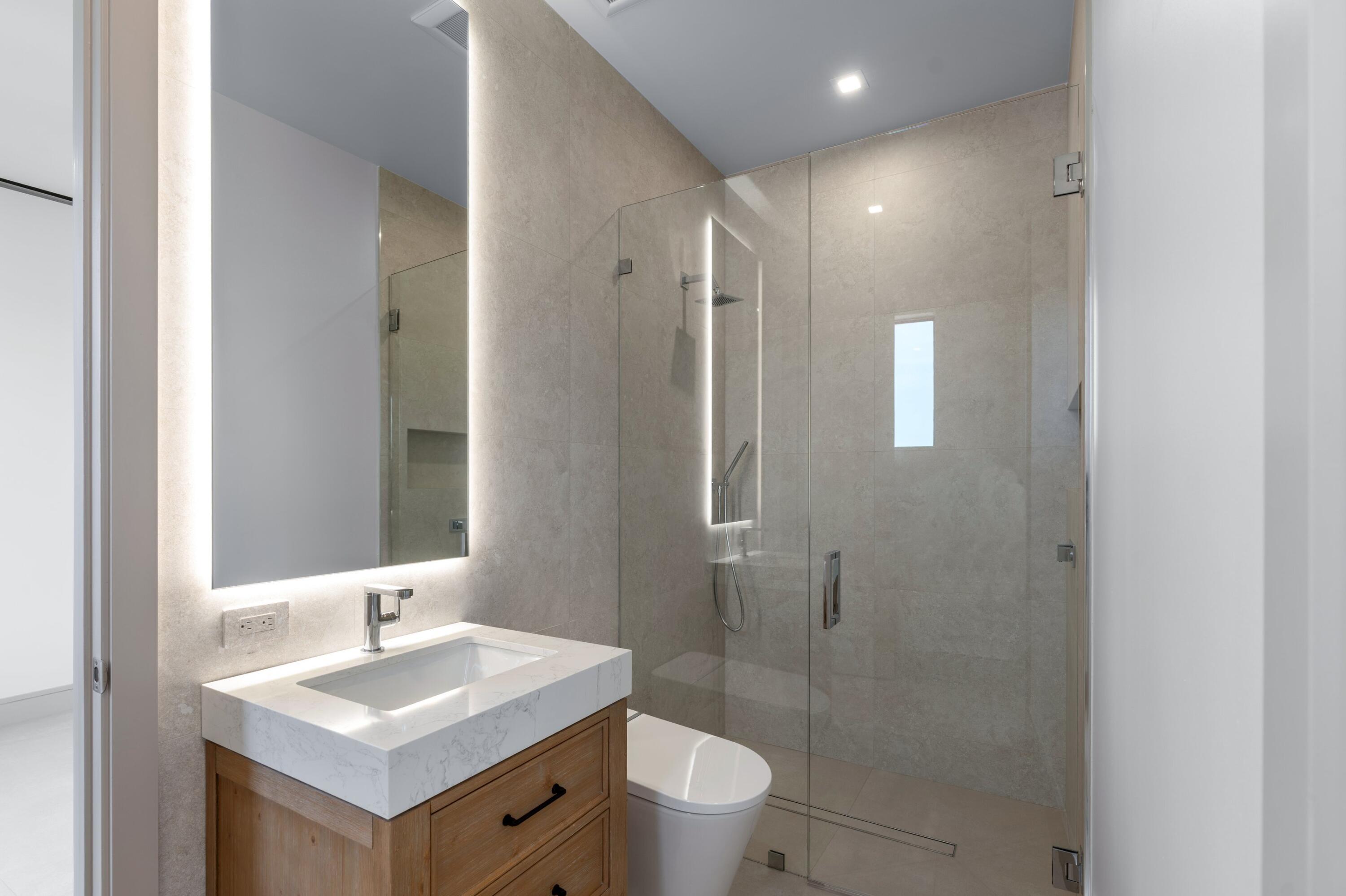 Modern bathroom with a wood vanity, illuminated mirror, and glass-enclosed shower.