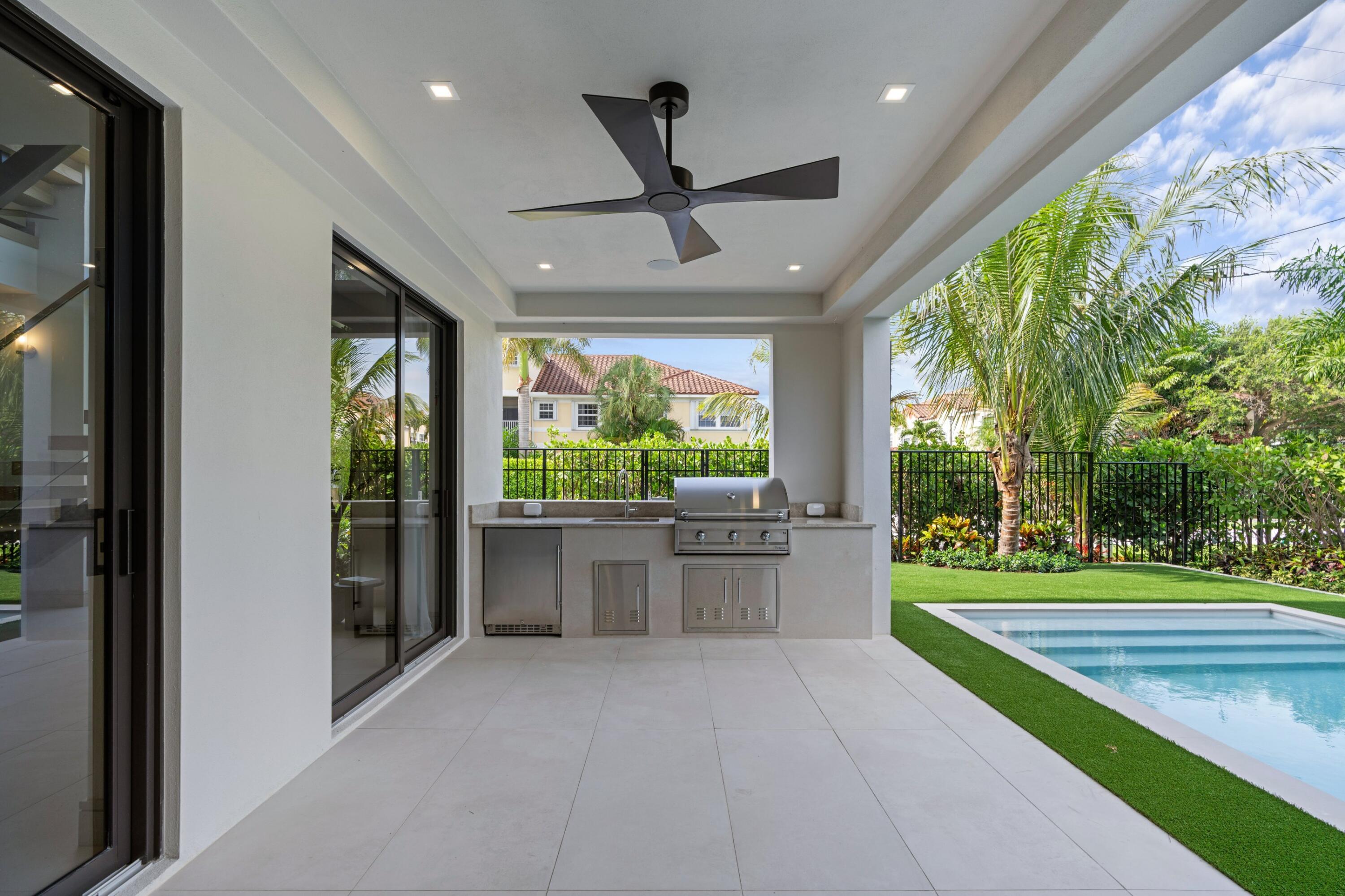Covered patio with built-in grill beside a swimming pool and tropical landscaping.