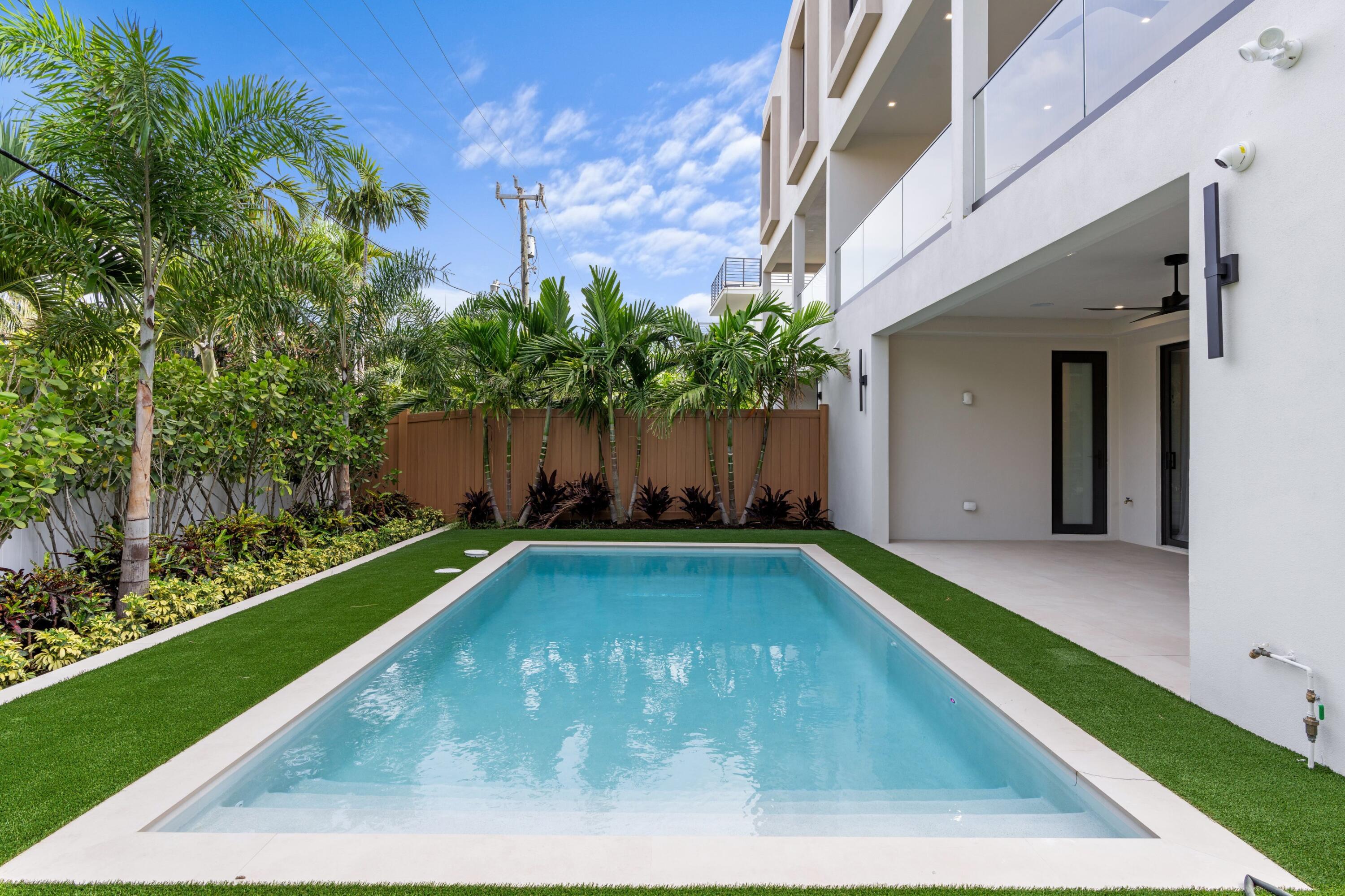 Rectangular swimming pool beside a modern home, with tropical palms and a covered patio.