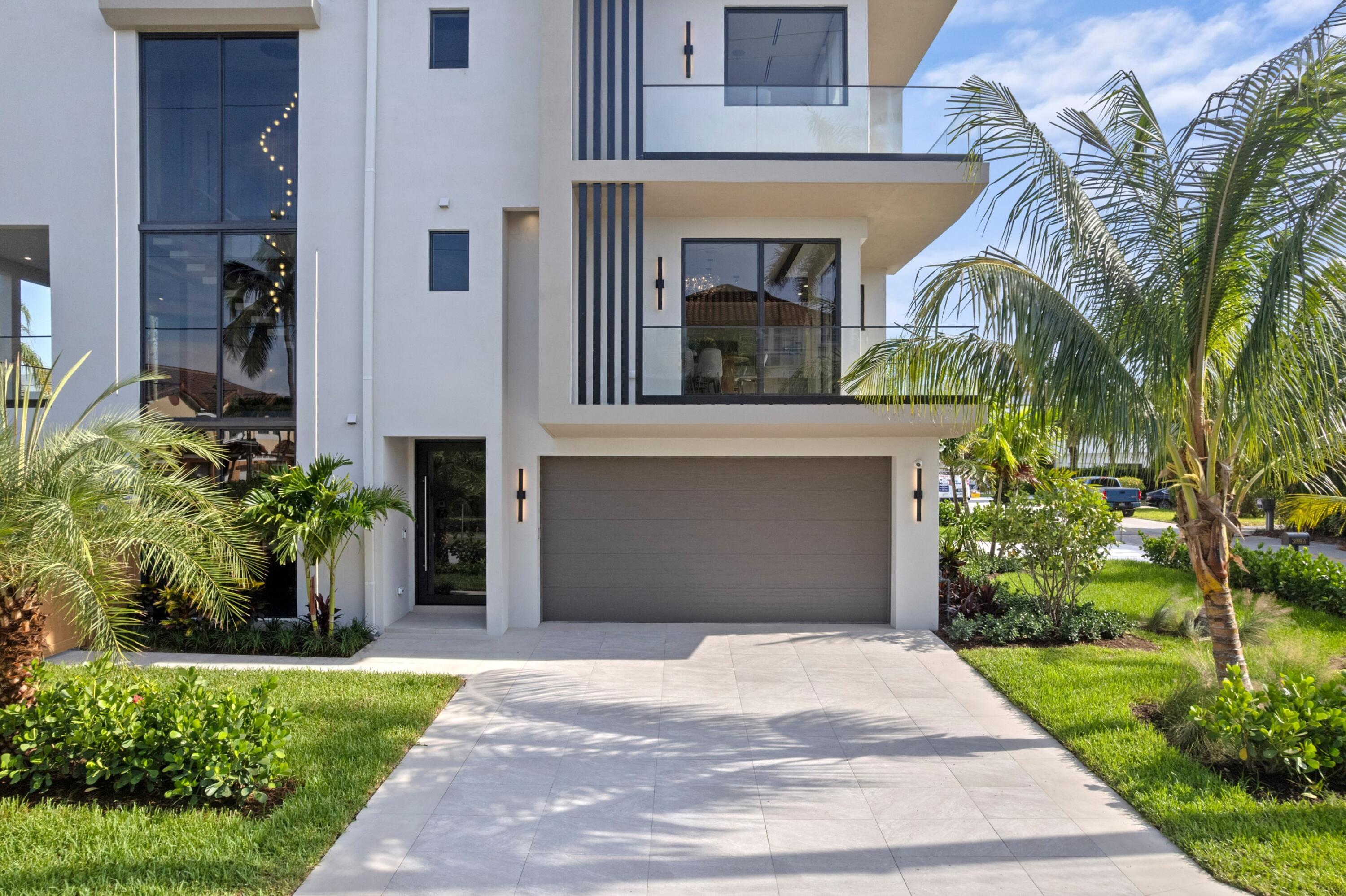 Modern white three-story home with glass balconies, a wide driveway, and tropical landscaping.