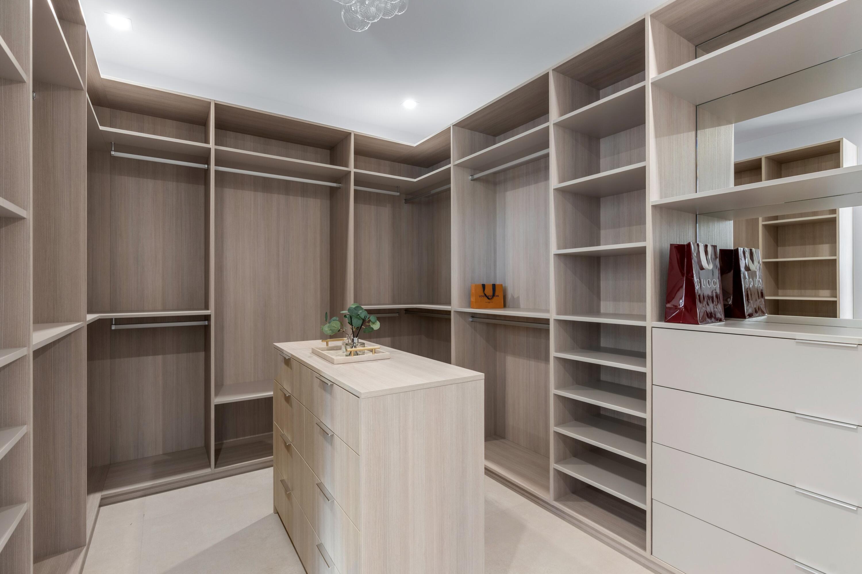 Walk-in closet with wood shelving, a central island, mirrored cabinetry, and designer shopping bags.