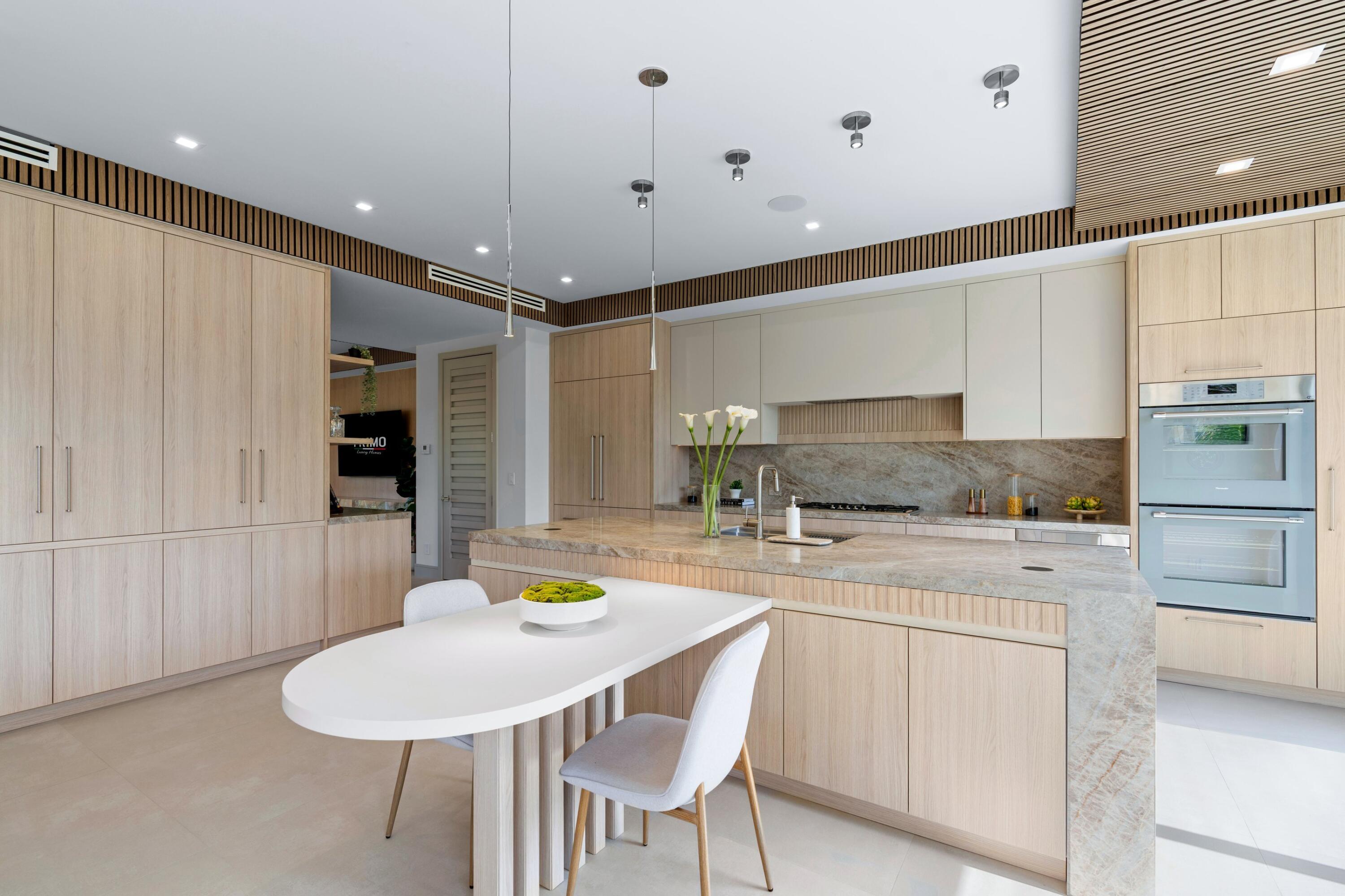 Modern kitchen with pale wood cabinetry, a marble island, and a white dining table.