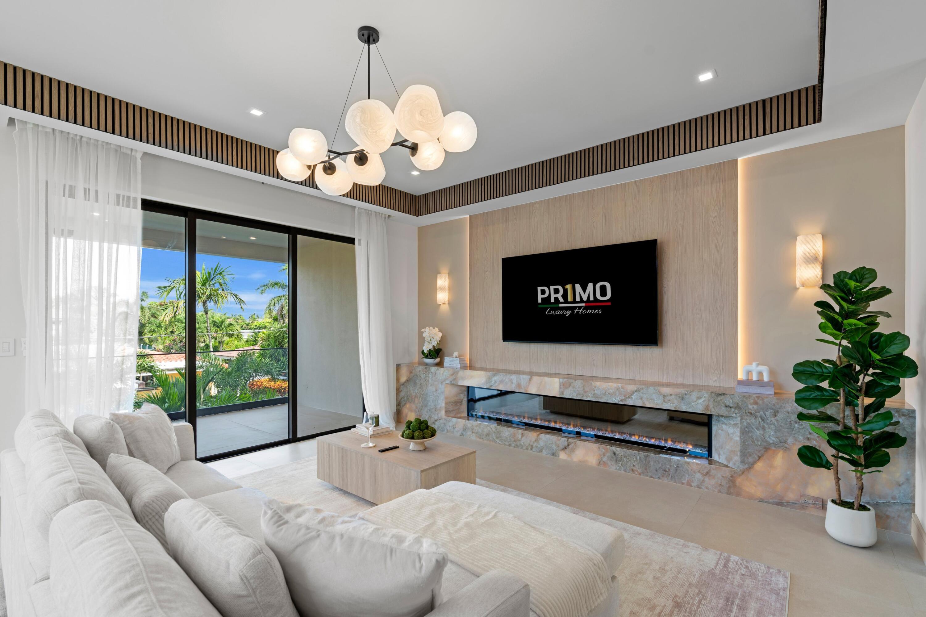 Living room with a white sectional, marble fireplace, wall-mounted TV, and sliding doors opening to tropical greenery.