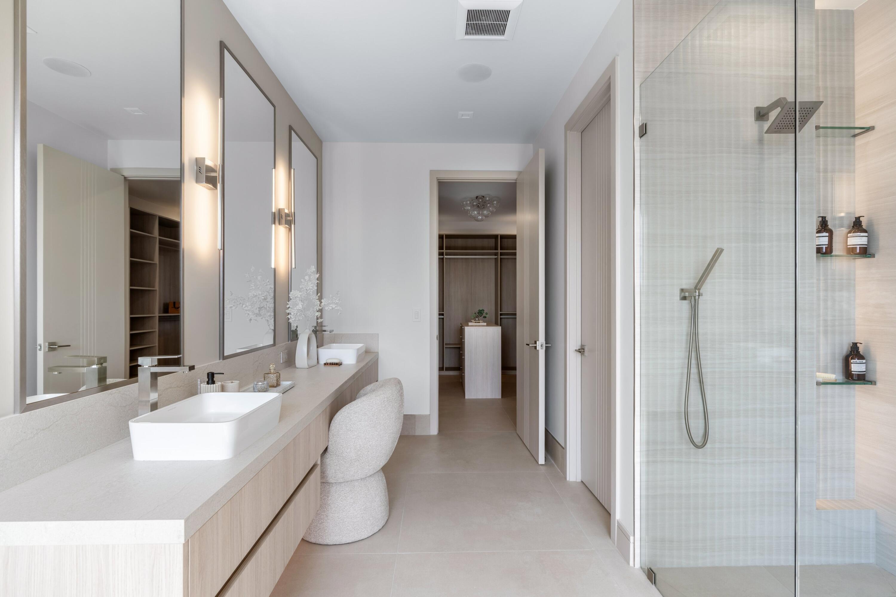 Bathroom with a double vanity, sculptural stools, and glass-enclosed shower.