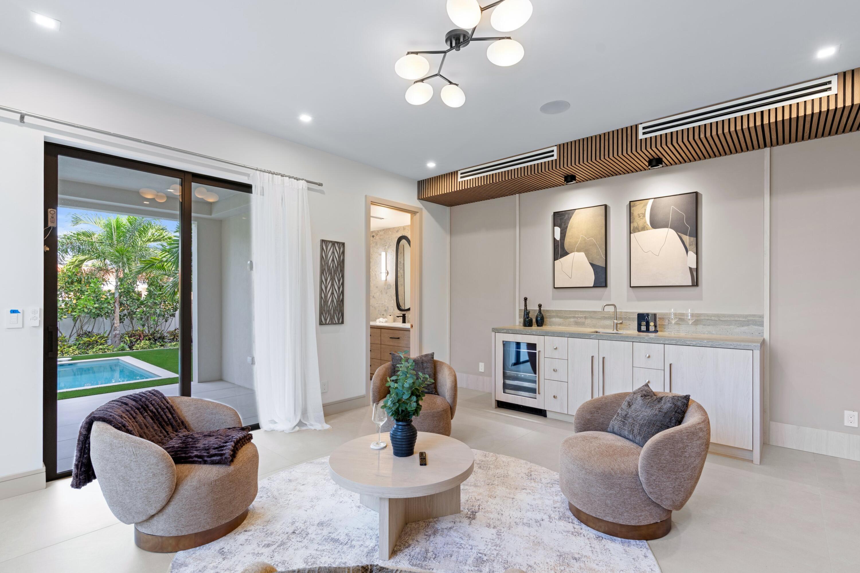 Sitting area with a built-in bar, sculptural chairs, and sliding doors opening to a poolside garden.