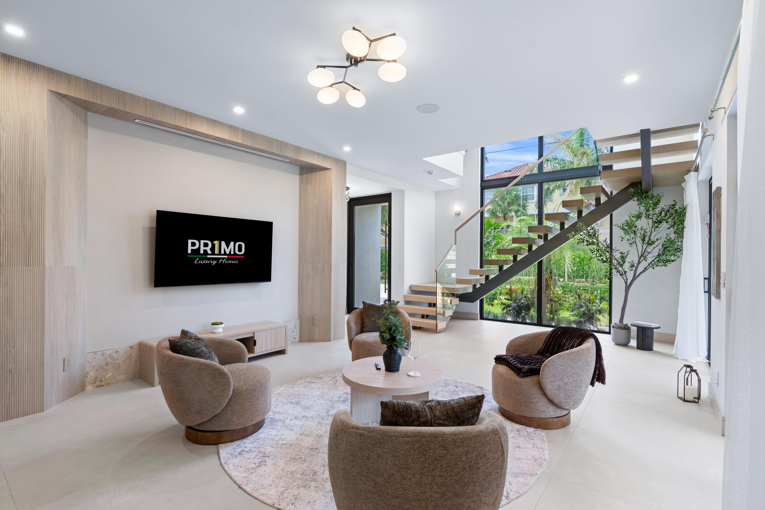 Bright living room with sculptural seating, a floating staircase, and floor-to-ceiling garden windows.