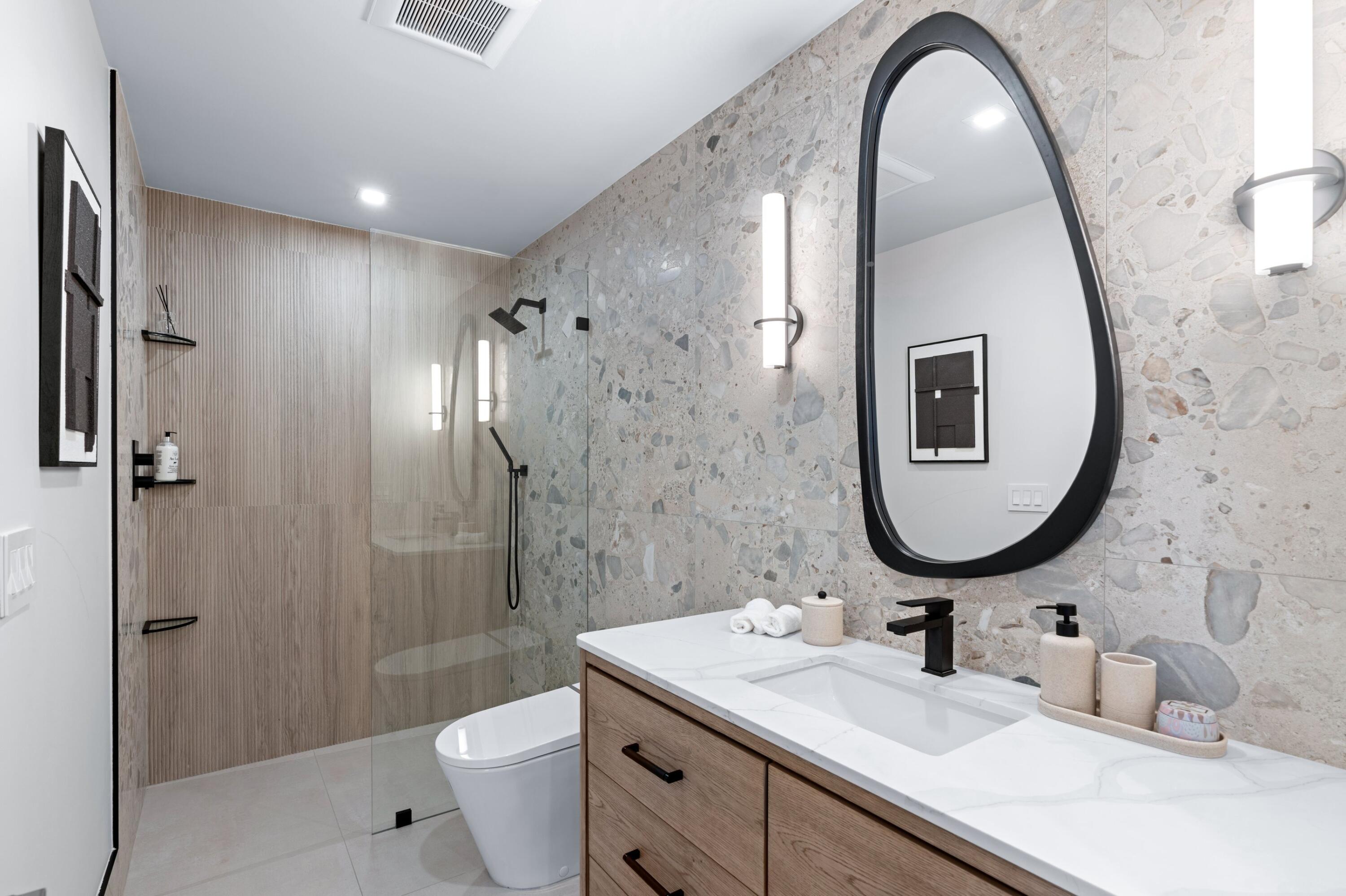 Modern bathroom with a glass-enclosed shower, stone walls, and a wood vanity.