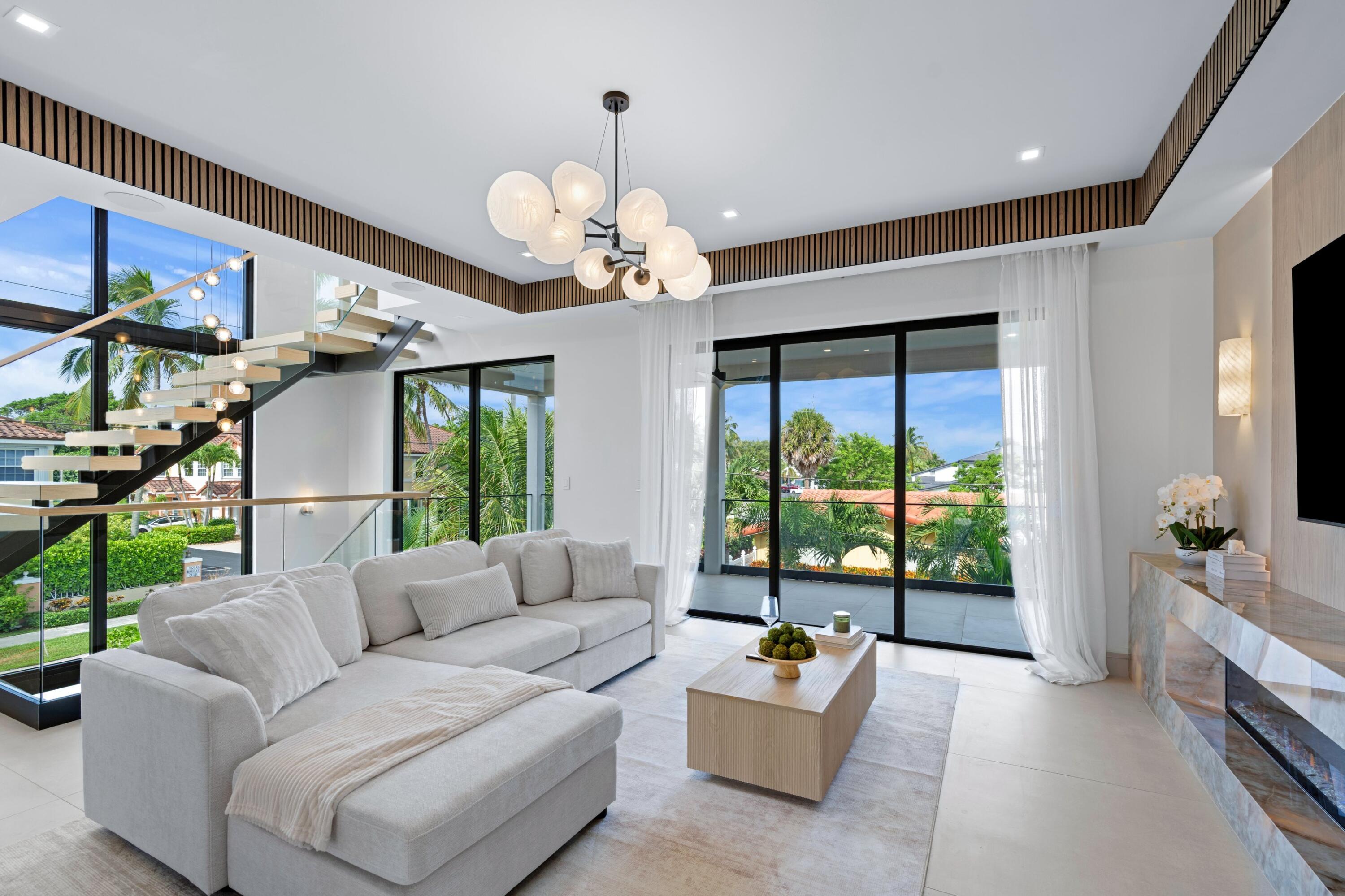 Staged living room with a sculptural staircase, floor-to-ceiling windows, and a large white sectional.