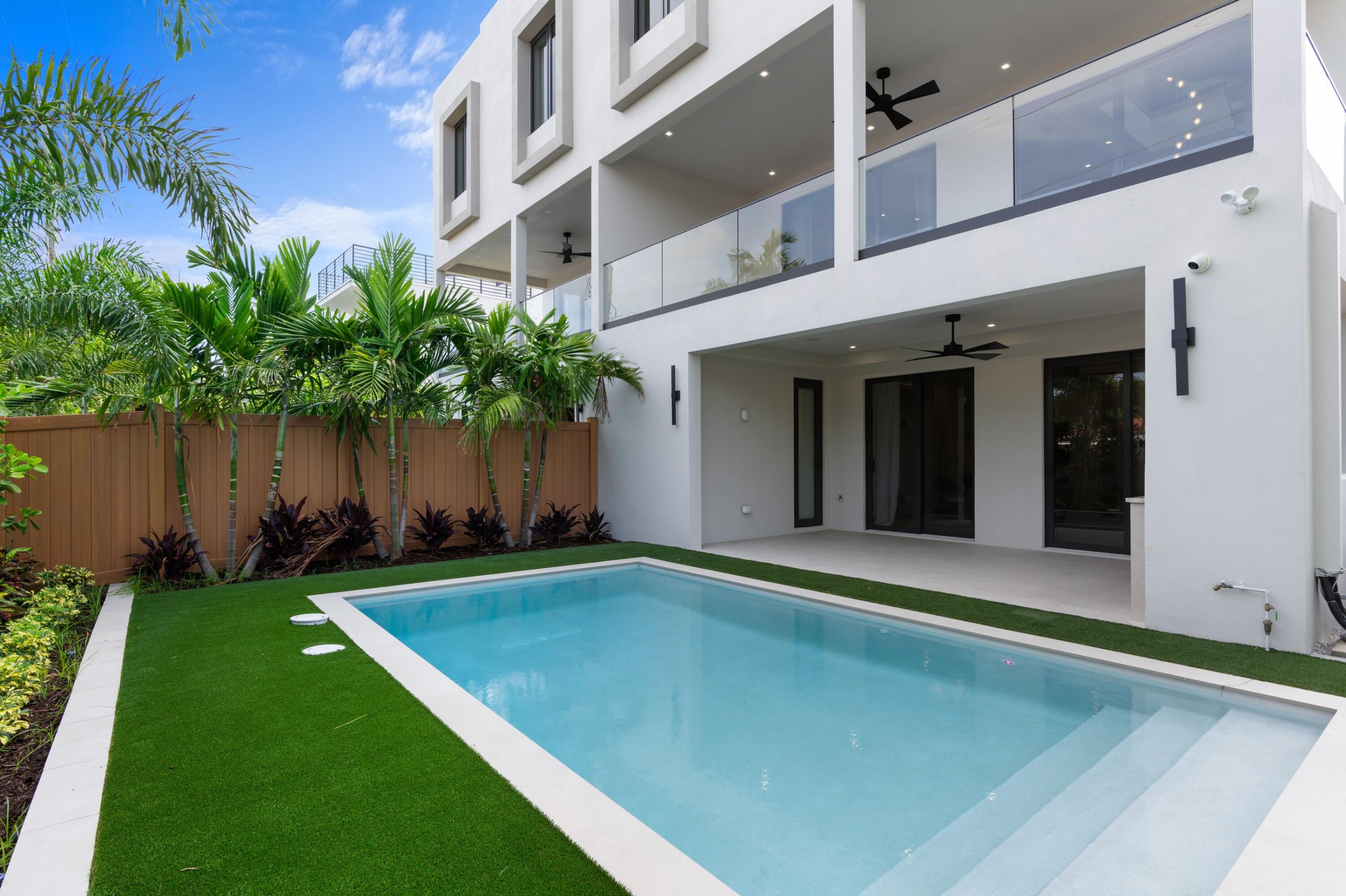 Modern white home with a rectangular pool, glass balconies, and tropical landscaping.
