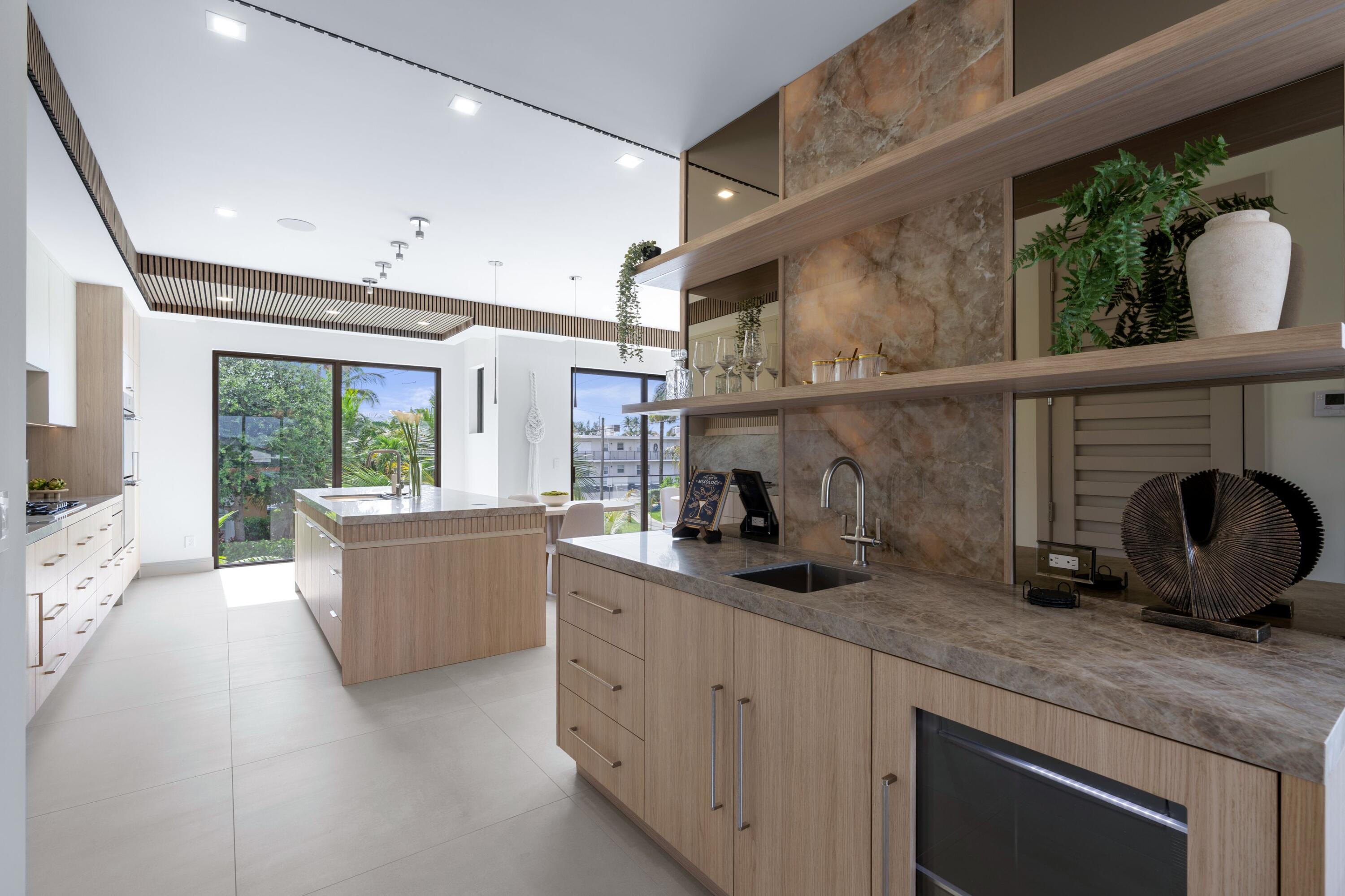 Modern kitchen with wood cabinetry, stone counters, a large island, and garden views through glass doors.